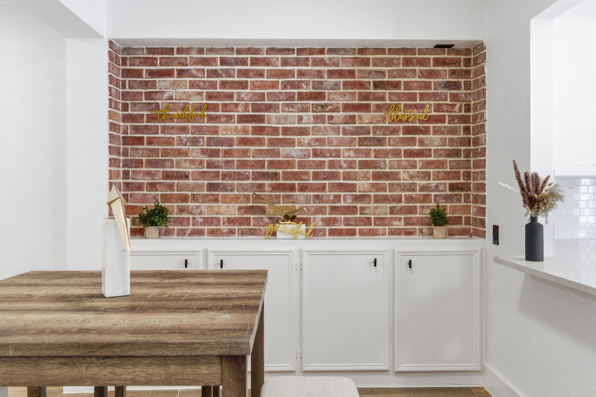 Exposed brick brings warmth and texture to the dining area while the cabinetry below adds practical storage. Exposed brick brings warmth and texture to the dining area while the cabinetry below adds practical storage.