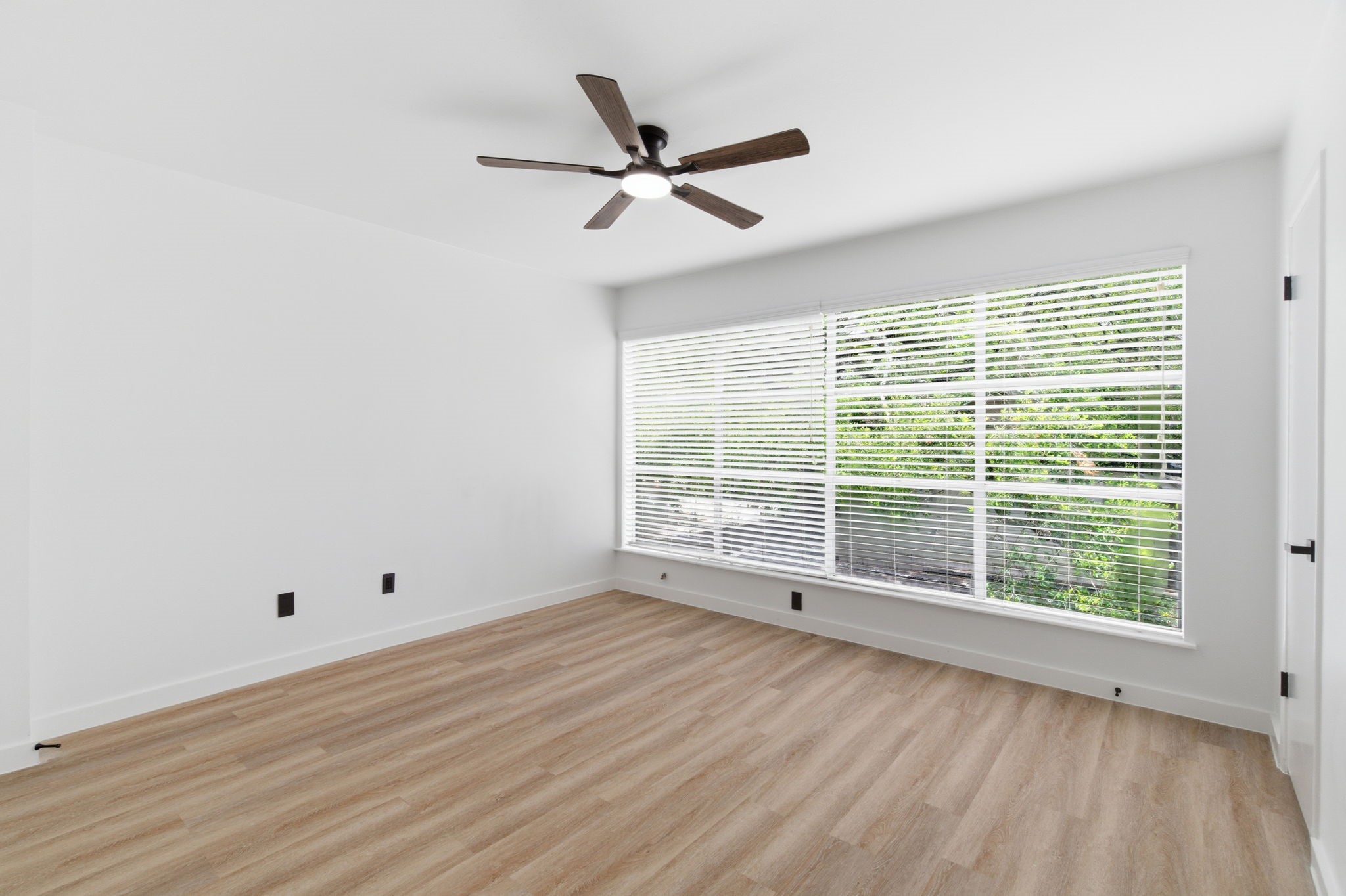 An oversized window stretches across the secondary bedroom, filling the space with natural light and views of the surrounding greenery.