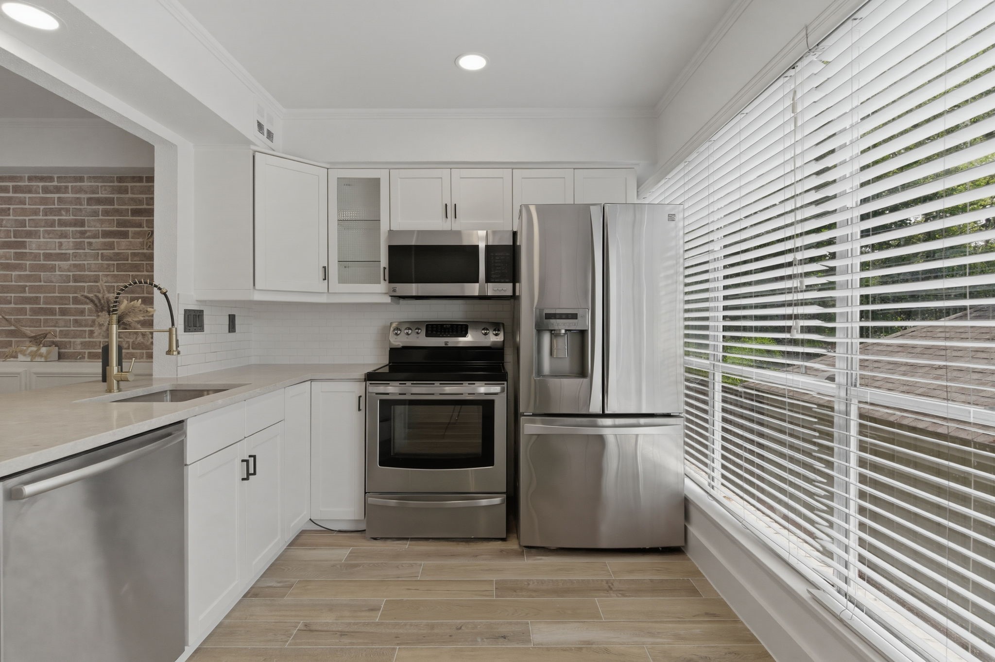 A wall of windows brings natural light into the kitchen and makes the white cabinetry and stainless steel appliances feel even brighter.