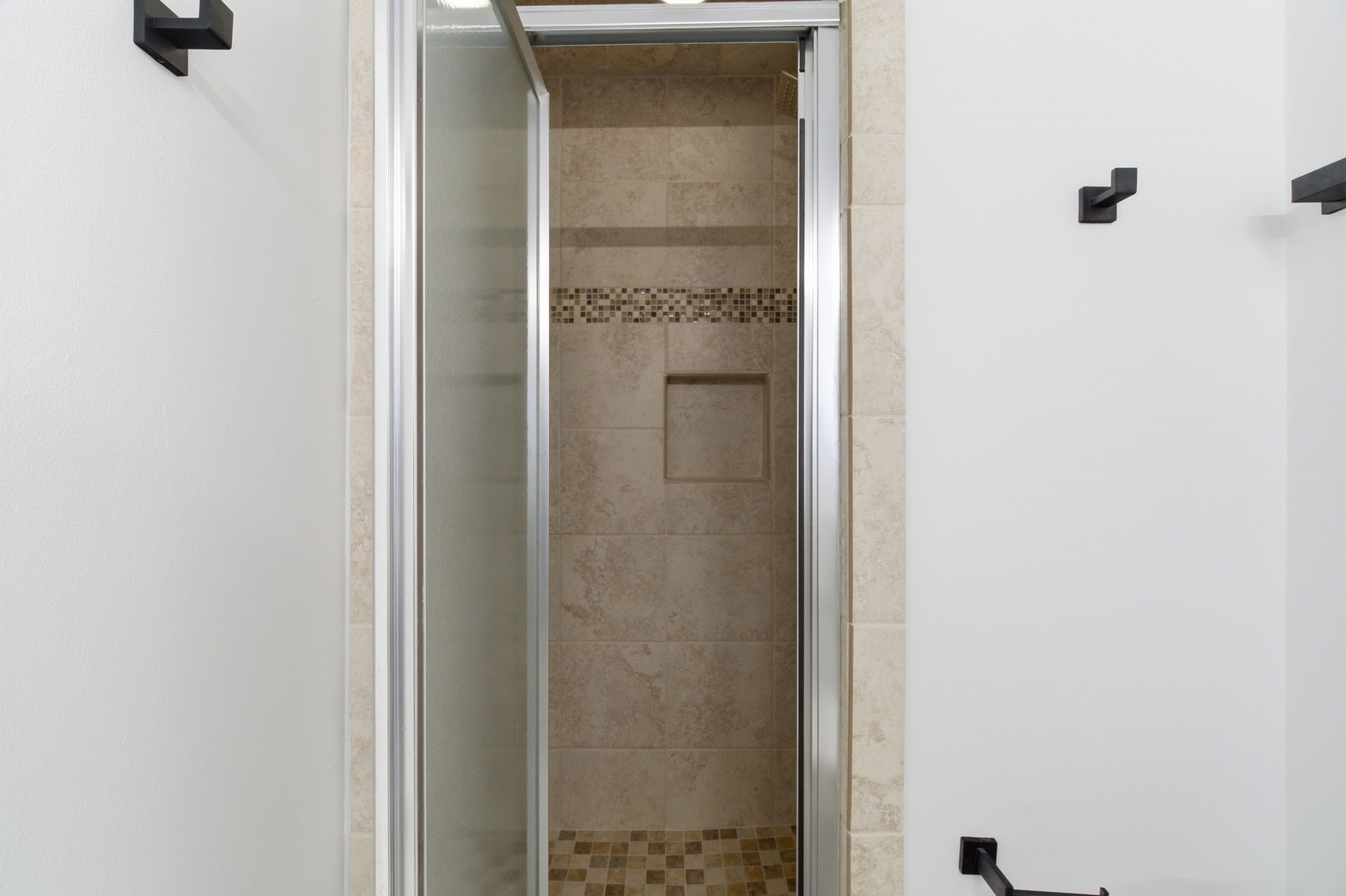 The tiled walk in shower features a decorative mosaic accent and a built in storage niche.