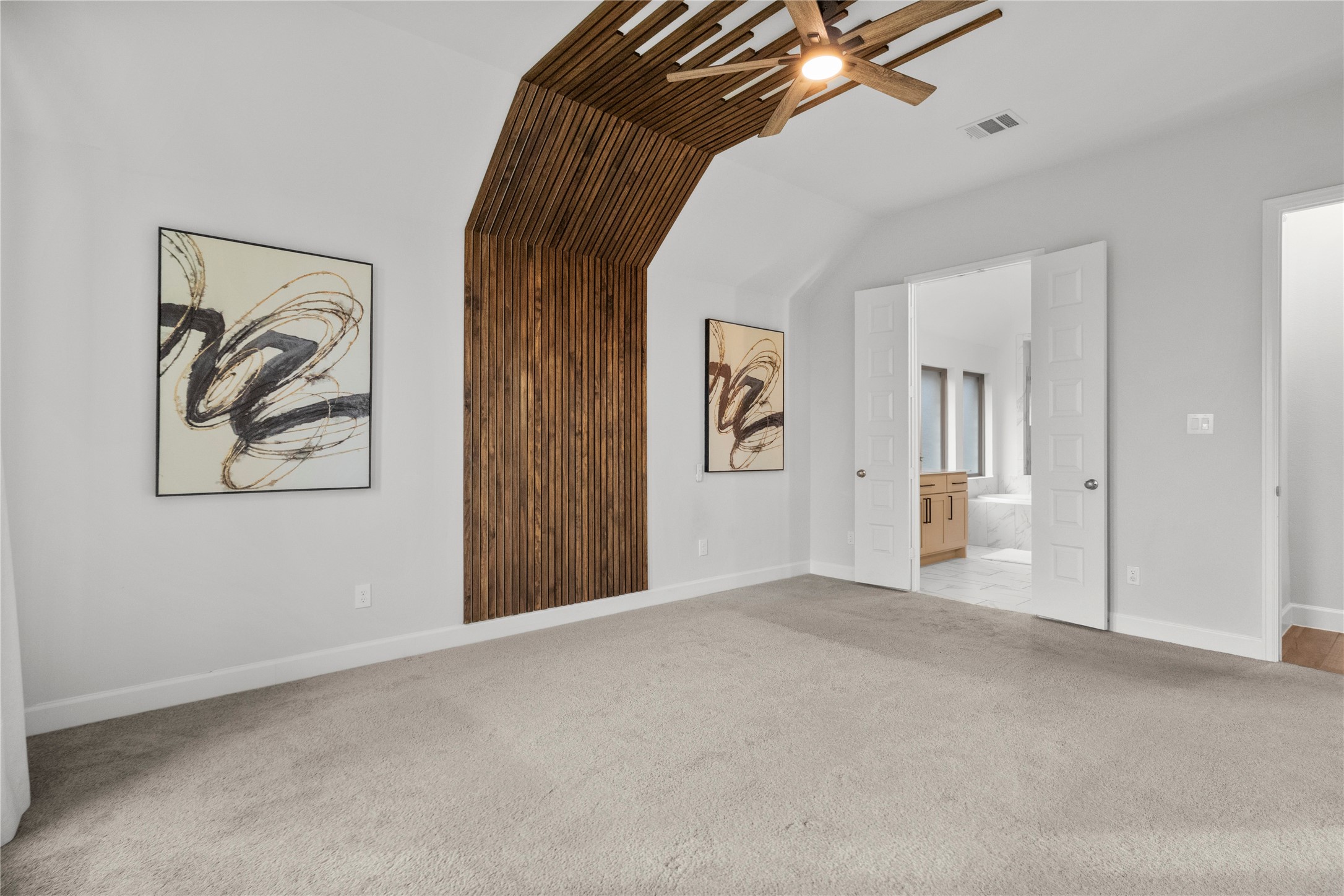 Spacious bedroom with a unique wood accent wall and modern ceiling fan, featuring double doors leading to a bright en-suite bathroom.