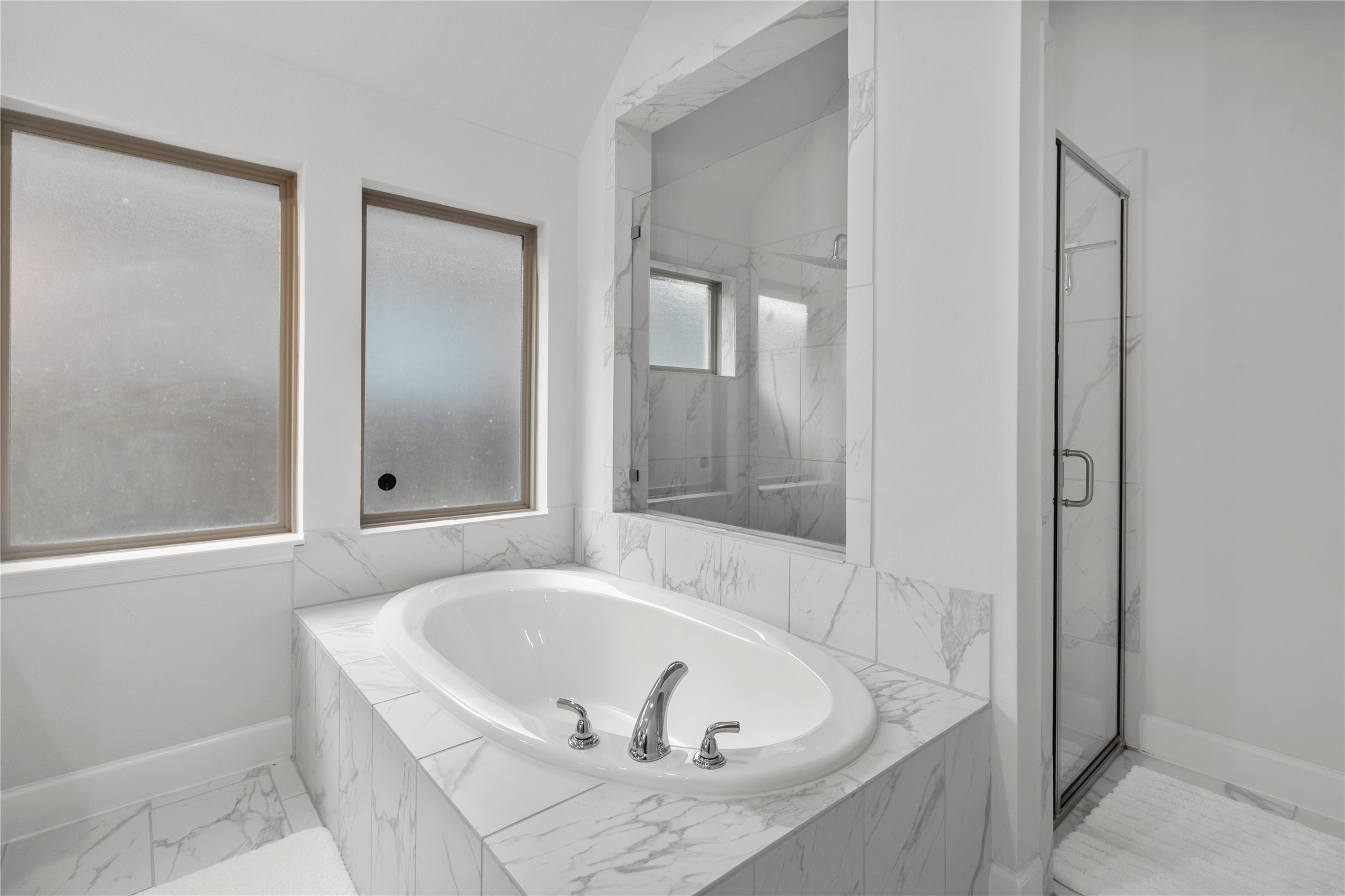 Elegant bathroom featuring a luxurious marble-tiled soaking tub and a spacious glass-enclosed shower, complemented by frosted windows for privacy and natural light.
