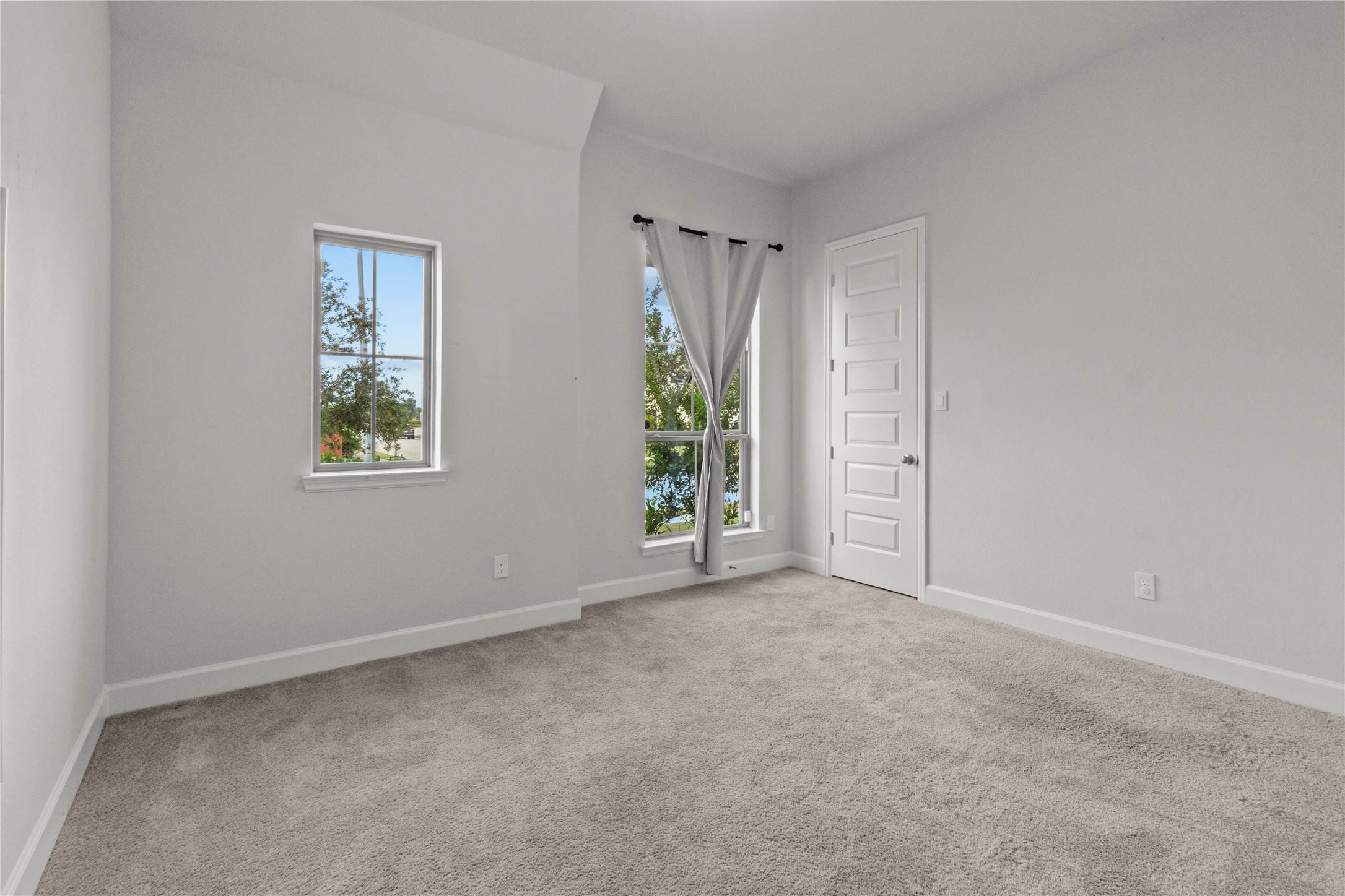 Bright and airy room with plush carpeting, large windows for natural light, and a modern white door. Bedroom1