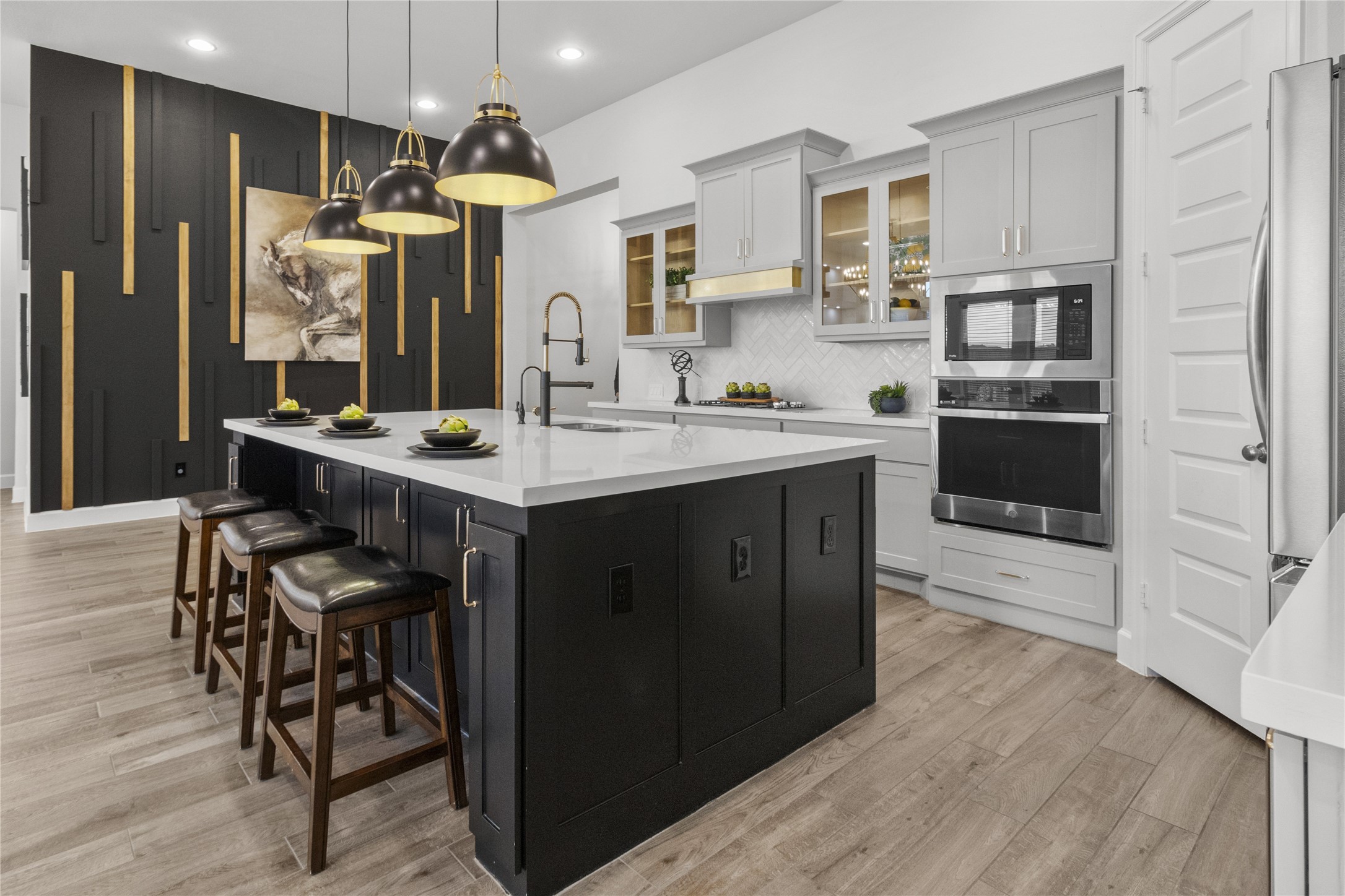 Sleek and modern kitchen with a large island, pendant lighting, and stylish black and gold accents. The open layout features white cabinetry, stainless steel appliances, and a sophisticated backsplash.