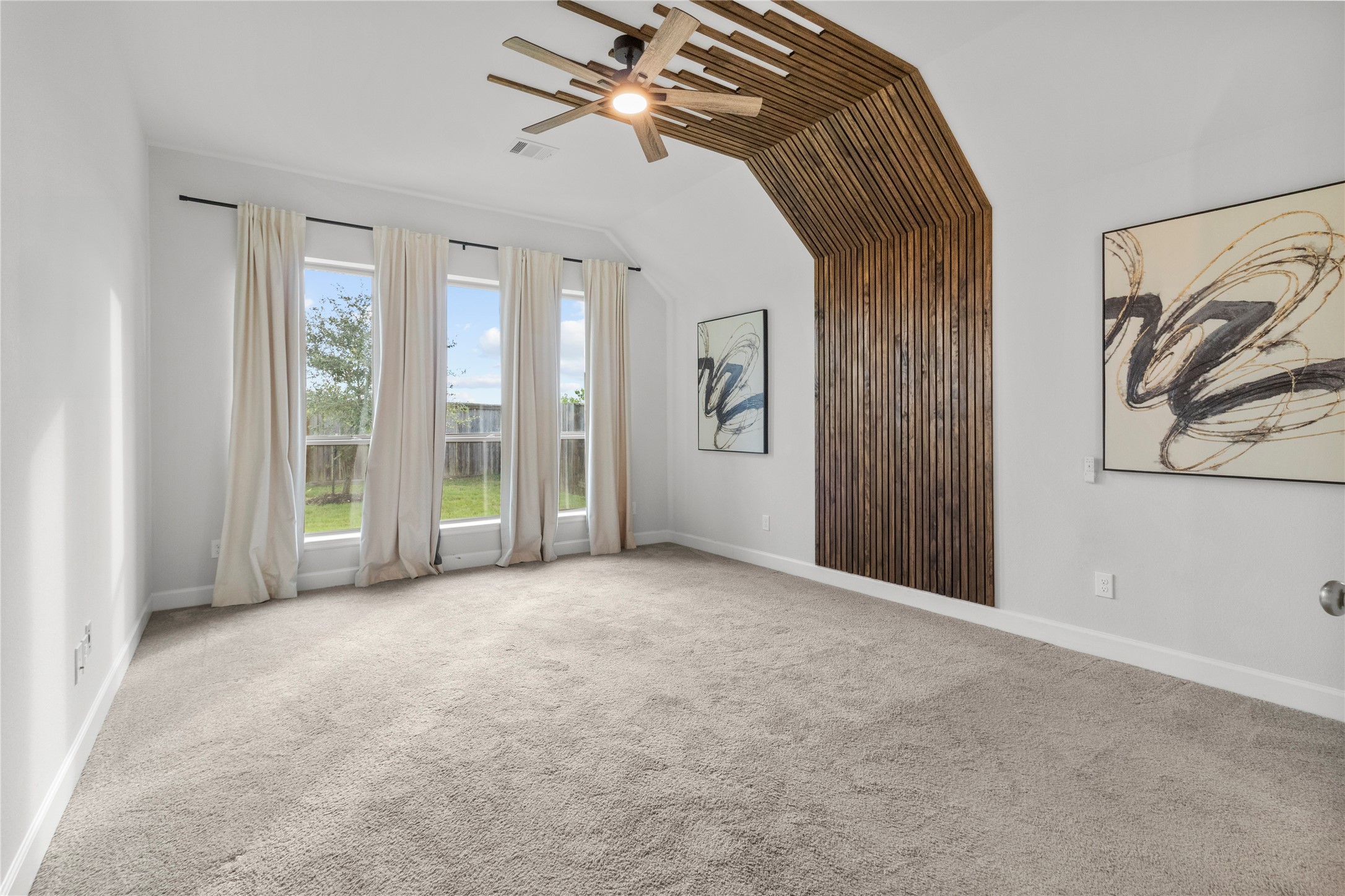 Spacious room with large windows offering abundant natural light, featuring a unique wood accent wall and modern ceiling fan, perfect for a stylish retreat. Primary Bedroom