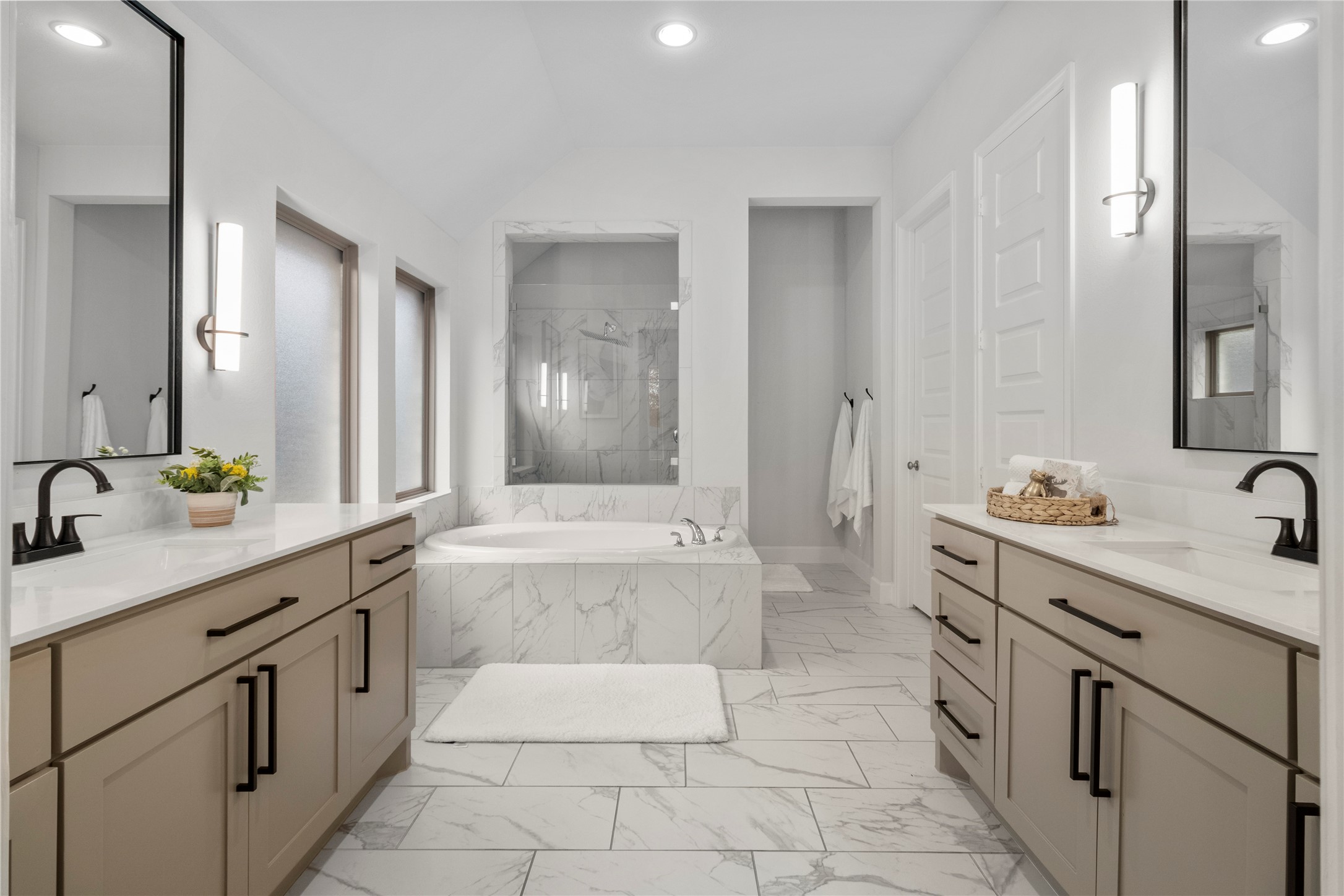 Luxurious bathroom featuring a spacious soaking tub, dual vanities with elegant fixtures, and modern lighting, all complemented by sleek tile flooring.