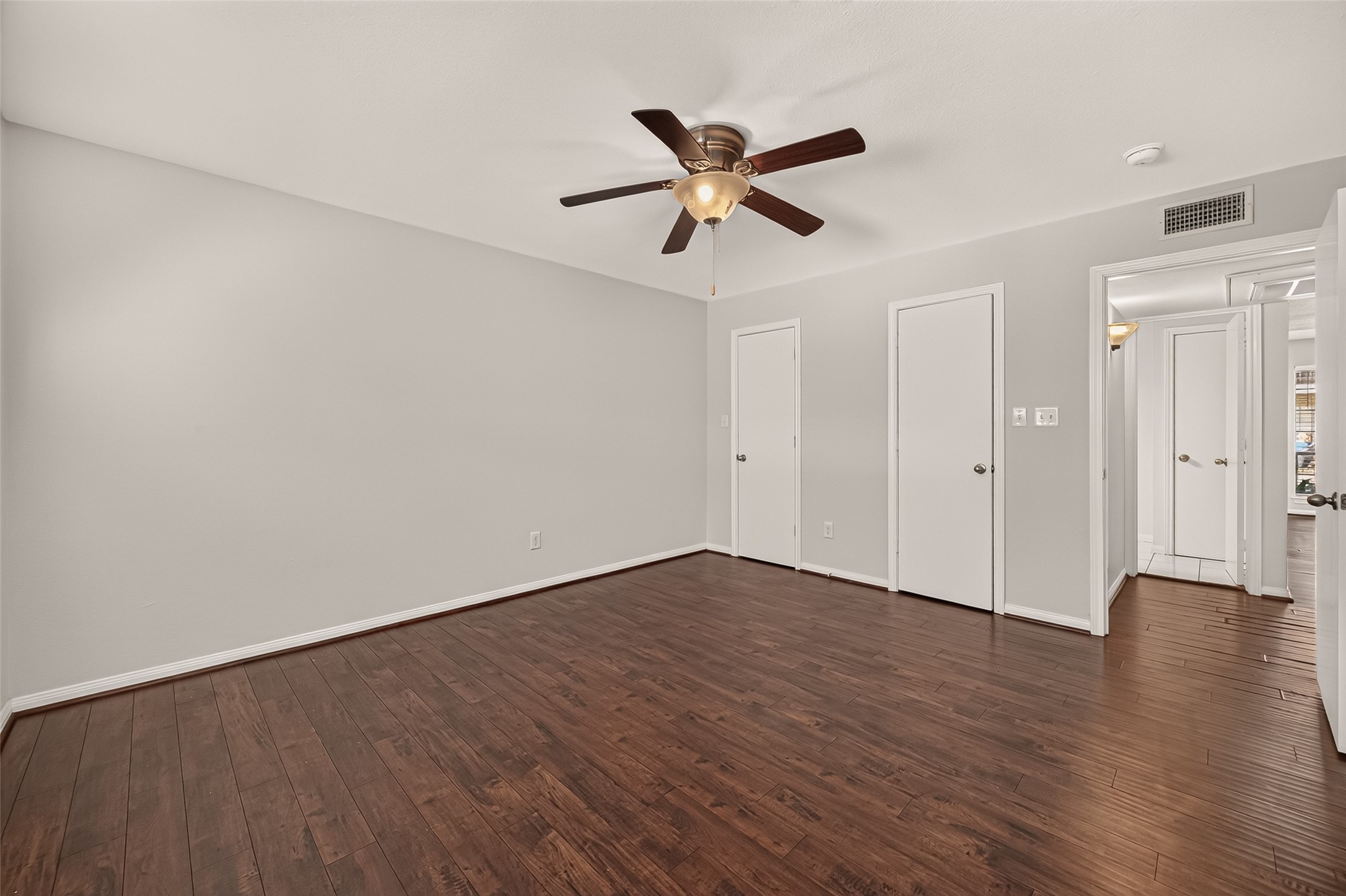 Spacious bedroom featuring rich wood flooring, a modern ceiling fan, and ample closet space, offering comfort and style.