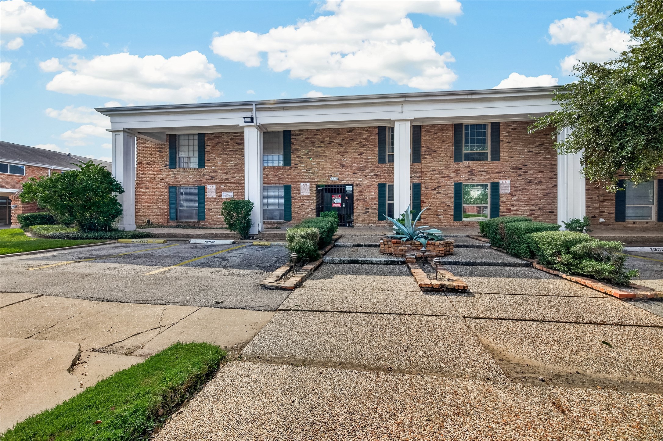 Charming brick building with classic columns and well-maintained landscaping, offering ample parking space and a welcoming entrance.