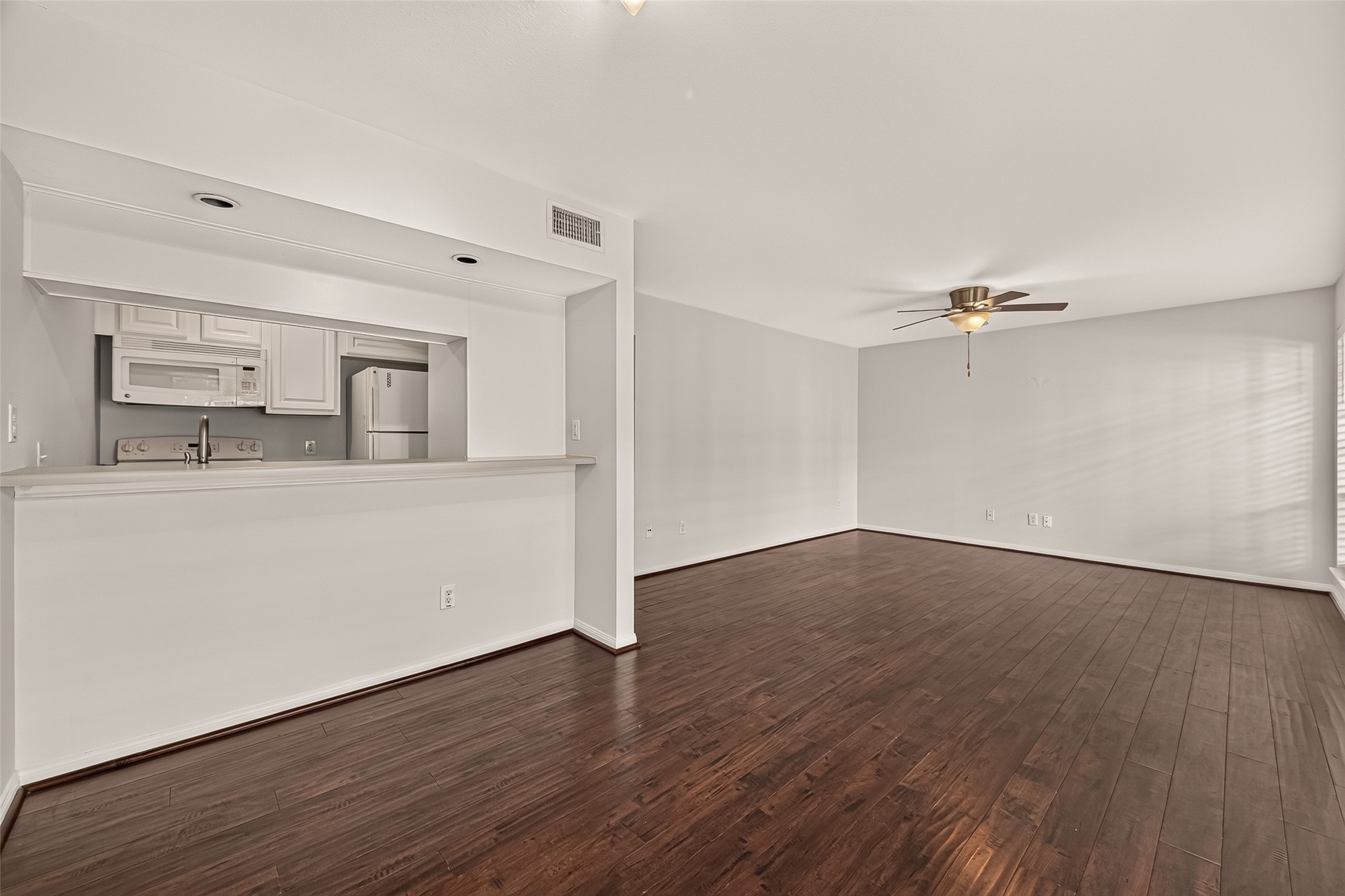 Spacious open-concept living area with elegant hardwood floors, a sleek ceiling fan, and a cozy kitchen pass-through for easy entertaining.