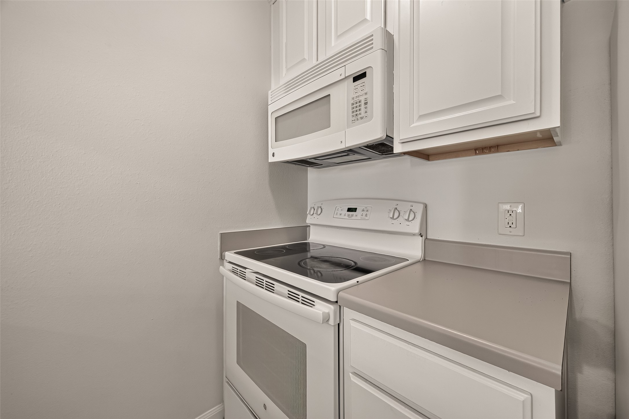 Modern kitchen corner featuring sleek white cabinetry, an electric stove, and a built-in microwave for convenience.