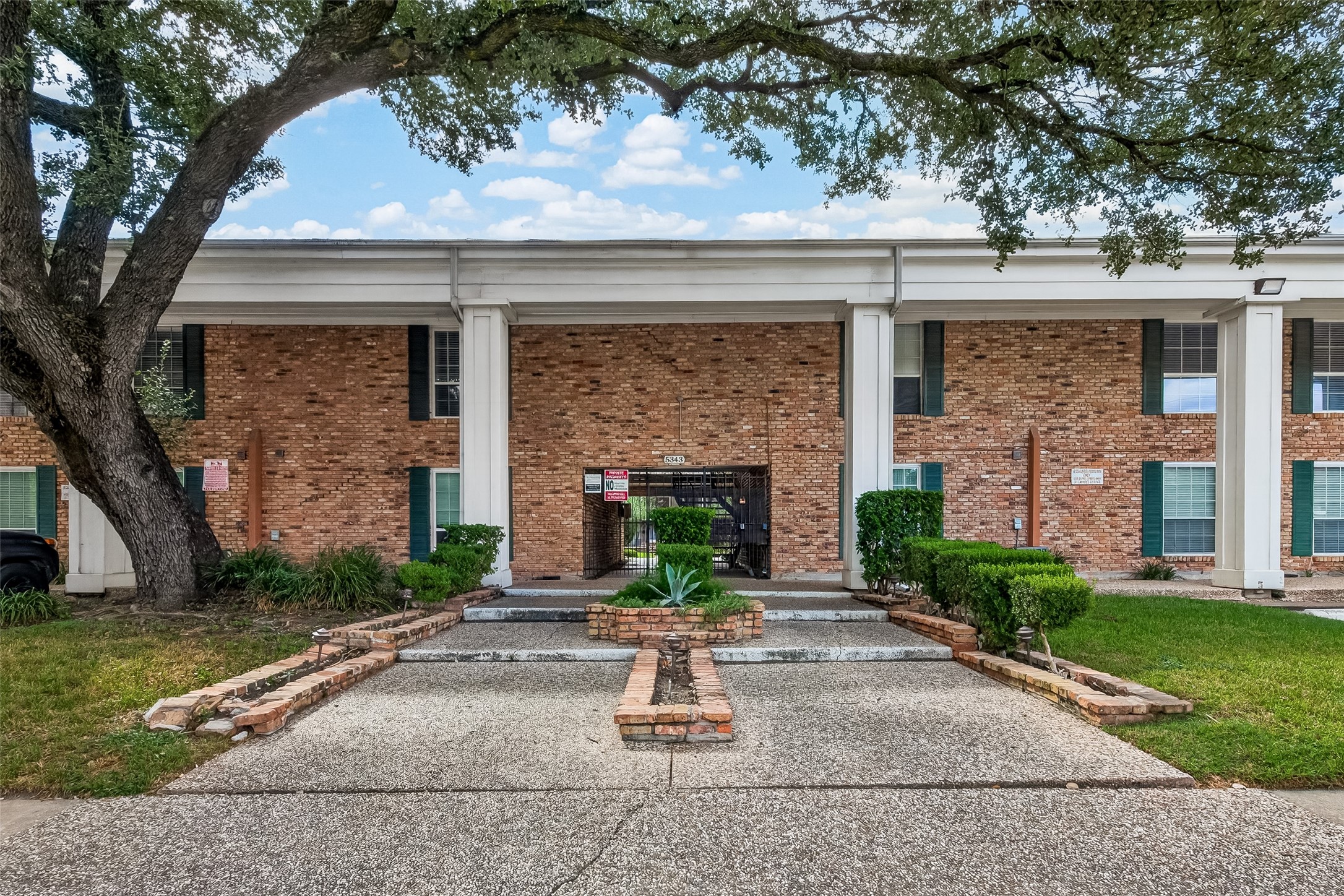 Charming brick townhouse with classic columns and lush landscaping, offering a welcoming entrance and a blend of traditional and modern appeal.