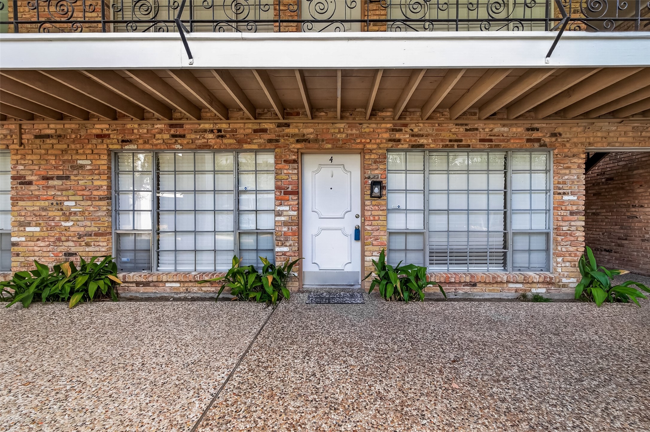 Charming brick exterior with large windows and a welcoming front door, complemented by elegant ironwork and lush greenery.