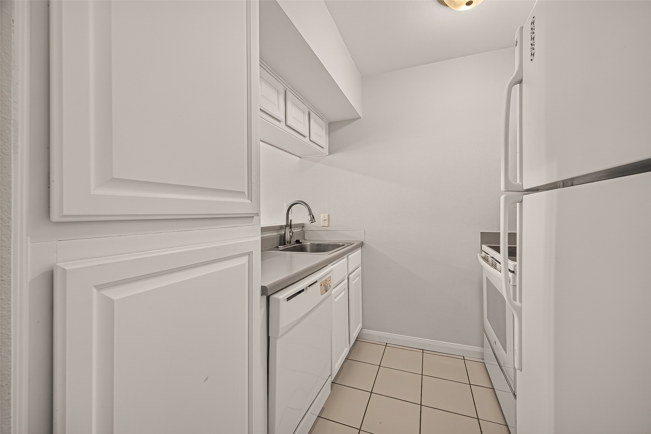 Charming galley kitchen with sleek white cabinets, tile flooring, and modern appliances, offering a clean and functional space.