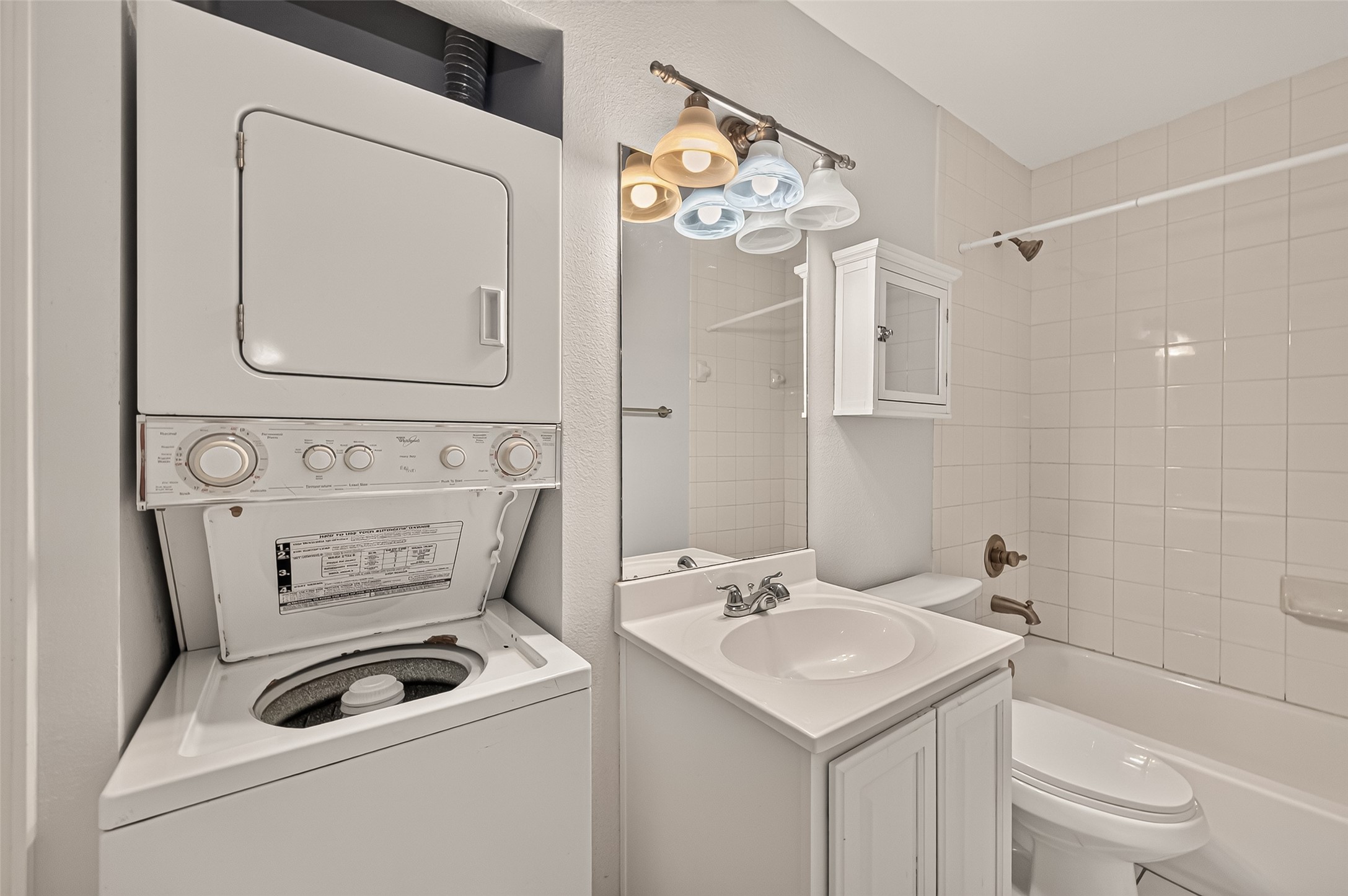 Compact bathroom with a convenient in-unit stacked washer and dryer, modern lighting, and a pristine tiled bathtub.