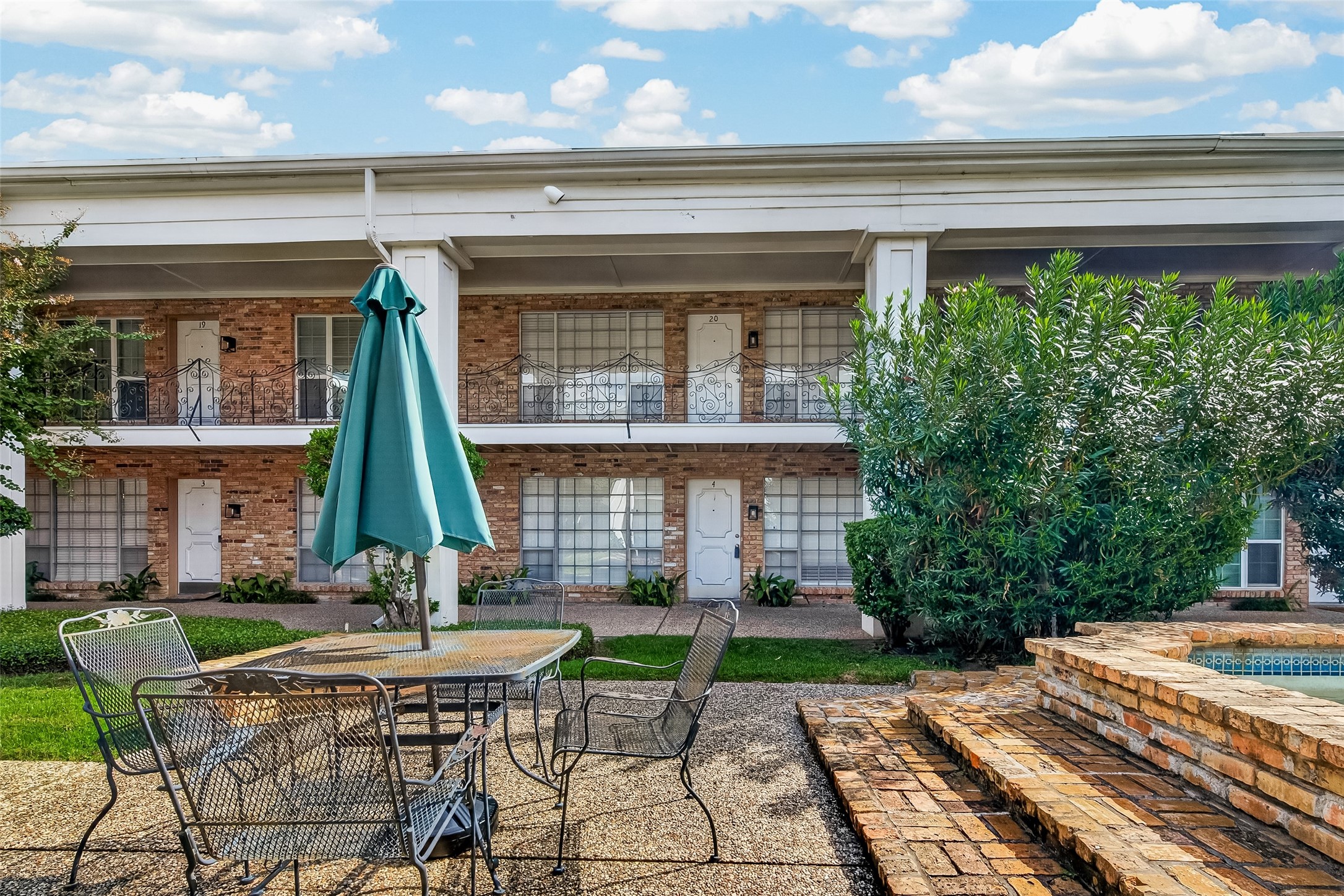Charming two-story brick home with classic ironwork details and inviting outdoor seating area, perfect for relaxation or entertaining.
