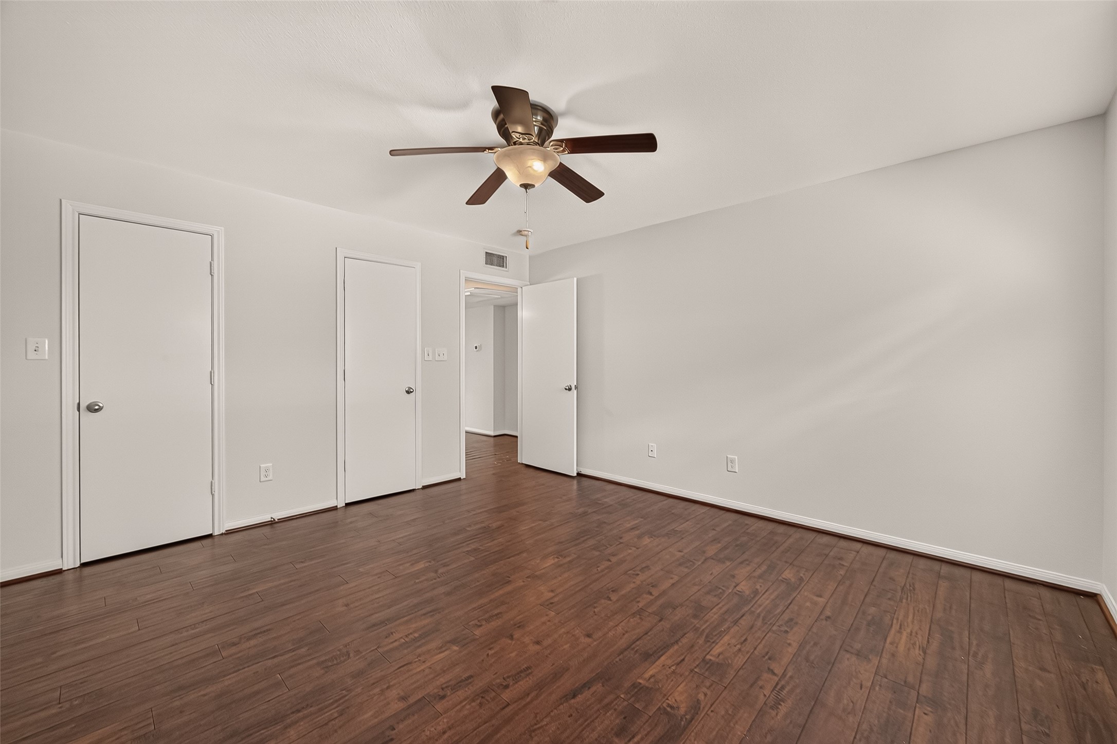 Spacious room featuring elegant hardwood flooring and a modern ceiling fan, complemented by neutral wall tones and multiple doorways for versatile use.