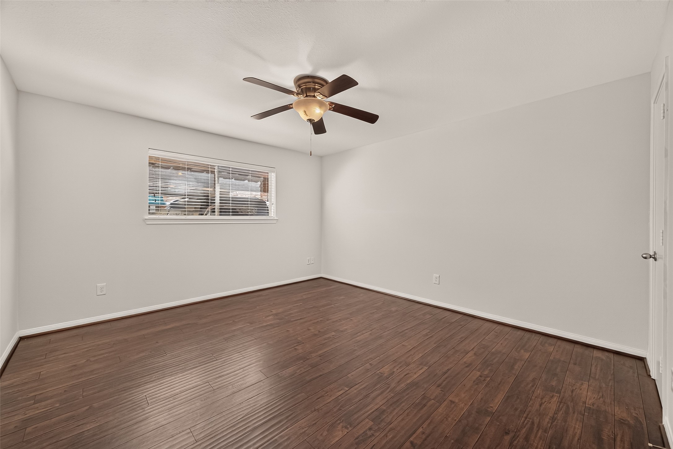 Spacious and bright room featuring elegant hardwood flooring, a modern ceiling fan, and a large window inviting natural light.