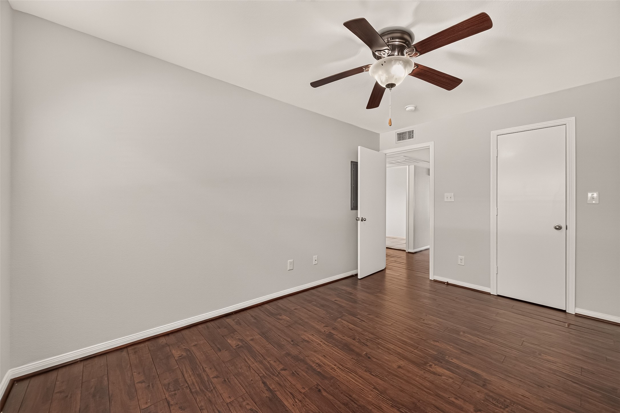 Spacious room with rich hardwood flooring, neutral walls, and a ceiling fan for added comfort.