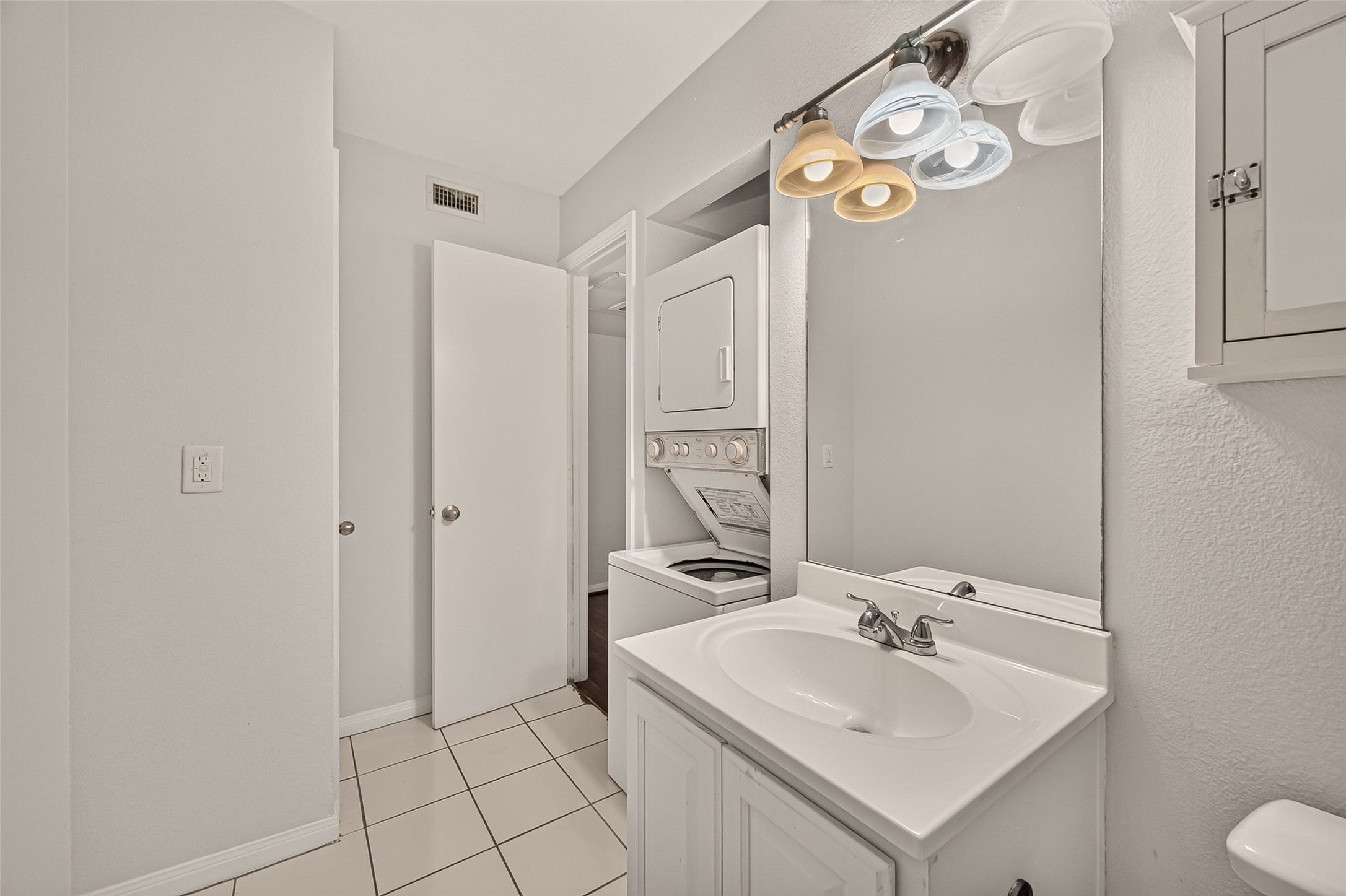 Bright and functional bathroom featuring a convenient in-unit washer and dryer, sleek vanity with modern lighting, and crisp white tile flooring.
