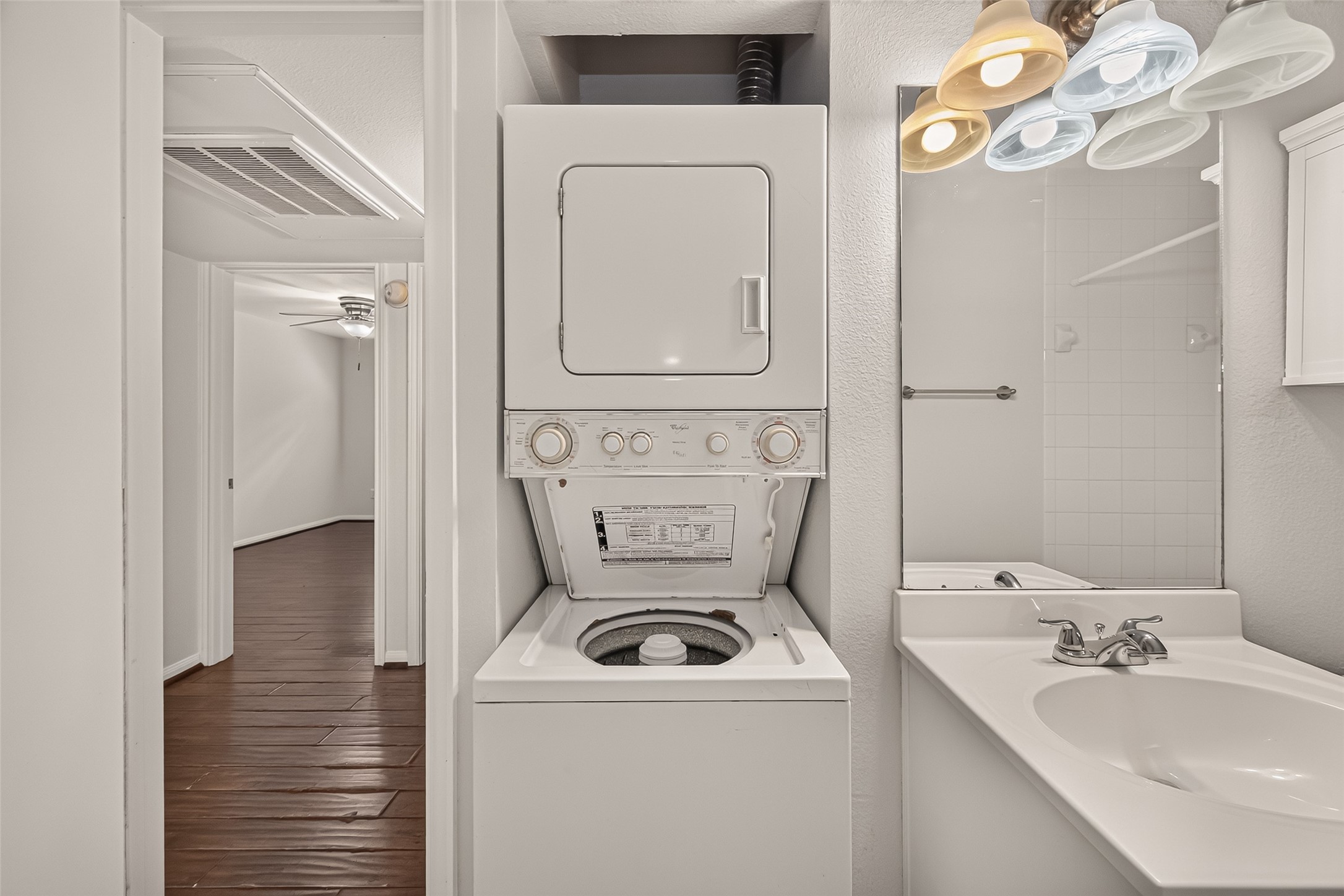 Convenient in-unit laundry features a stacked washer and dryer adjacent to a sleek bathroom with a modern vanity, all set against rich wood flooring.