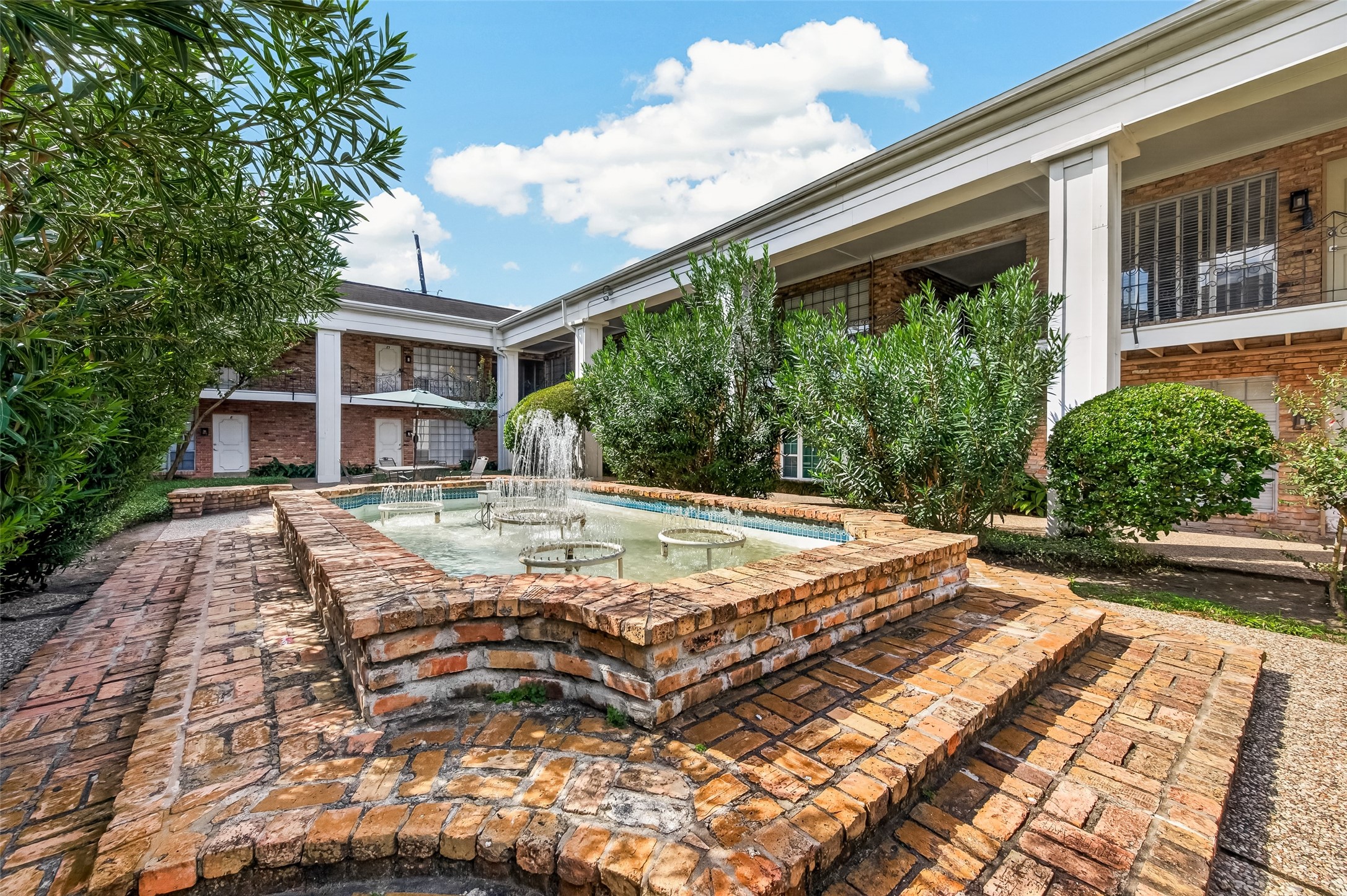 Charming brick courtyard featuring a central fountain and lush greenery, perfect for relaxing outdoors.