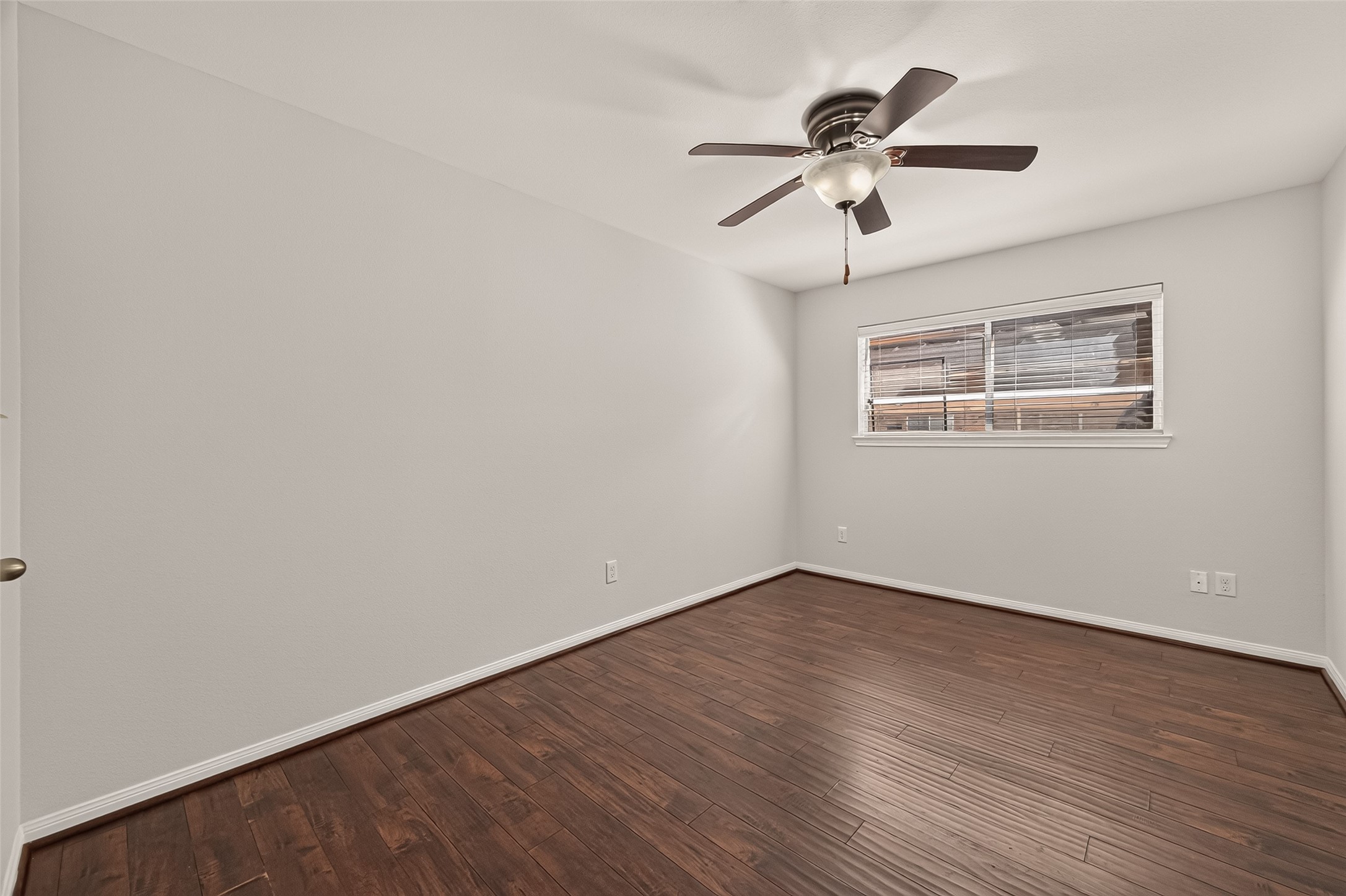 Spacious bedroom with rich wood flooring, a ceiling fan, and ample natural light from the large window.