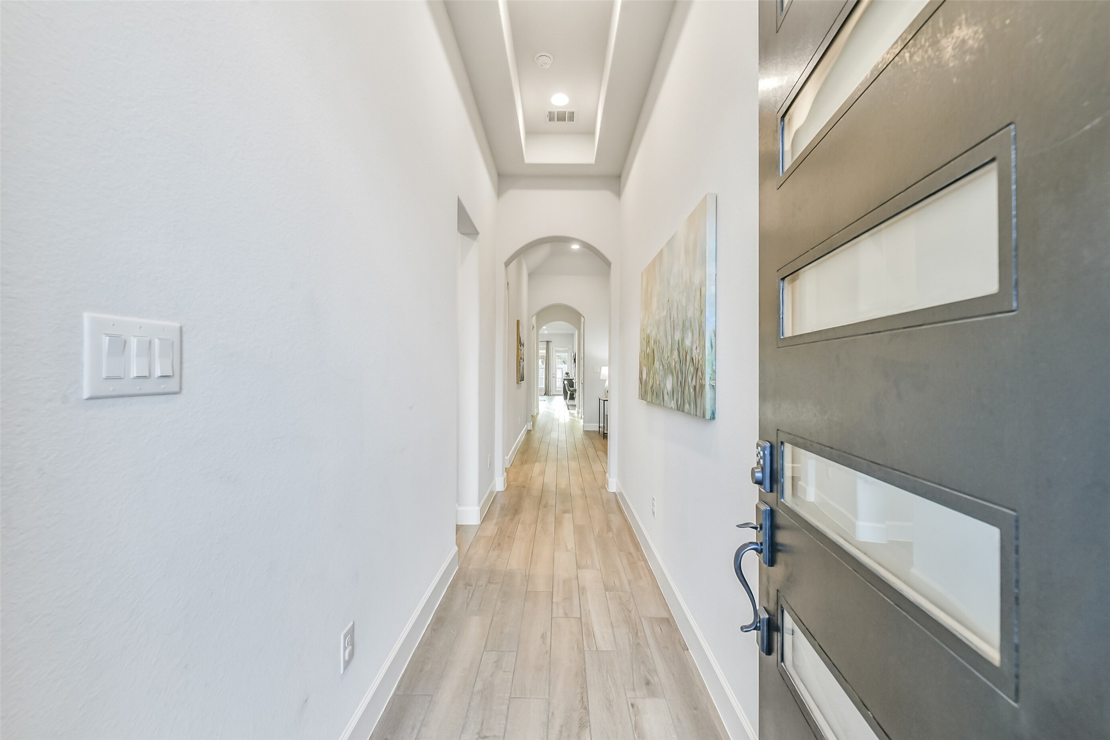 A wood and glass door opens to a beautiful hallway entry featuring high ceilings and gorgeous arched doorways.