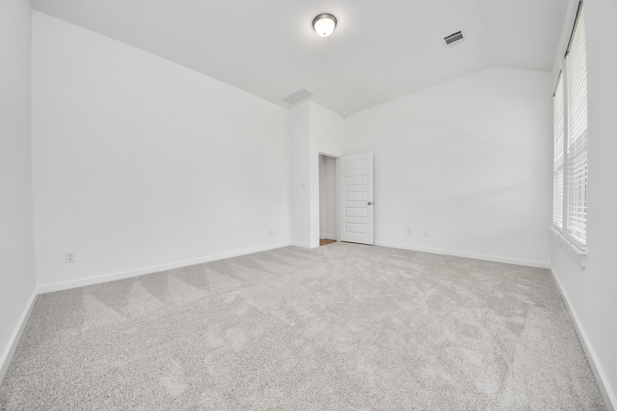 Escape and relax in the exquisite primary suite, a haven to unwind after a long day. The spacious room, located on first floor, boasts plush carpeting, soothing paint tones, high ceilings, and expansive windows adorned with privacy blinds. Sample photo of completed home with similar floor plan. Actual colors and selections may vary.