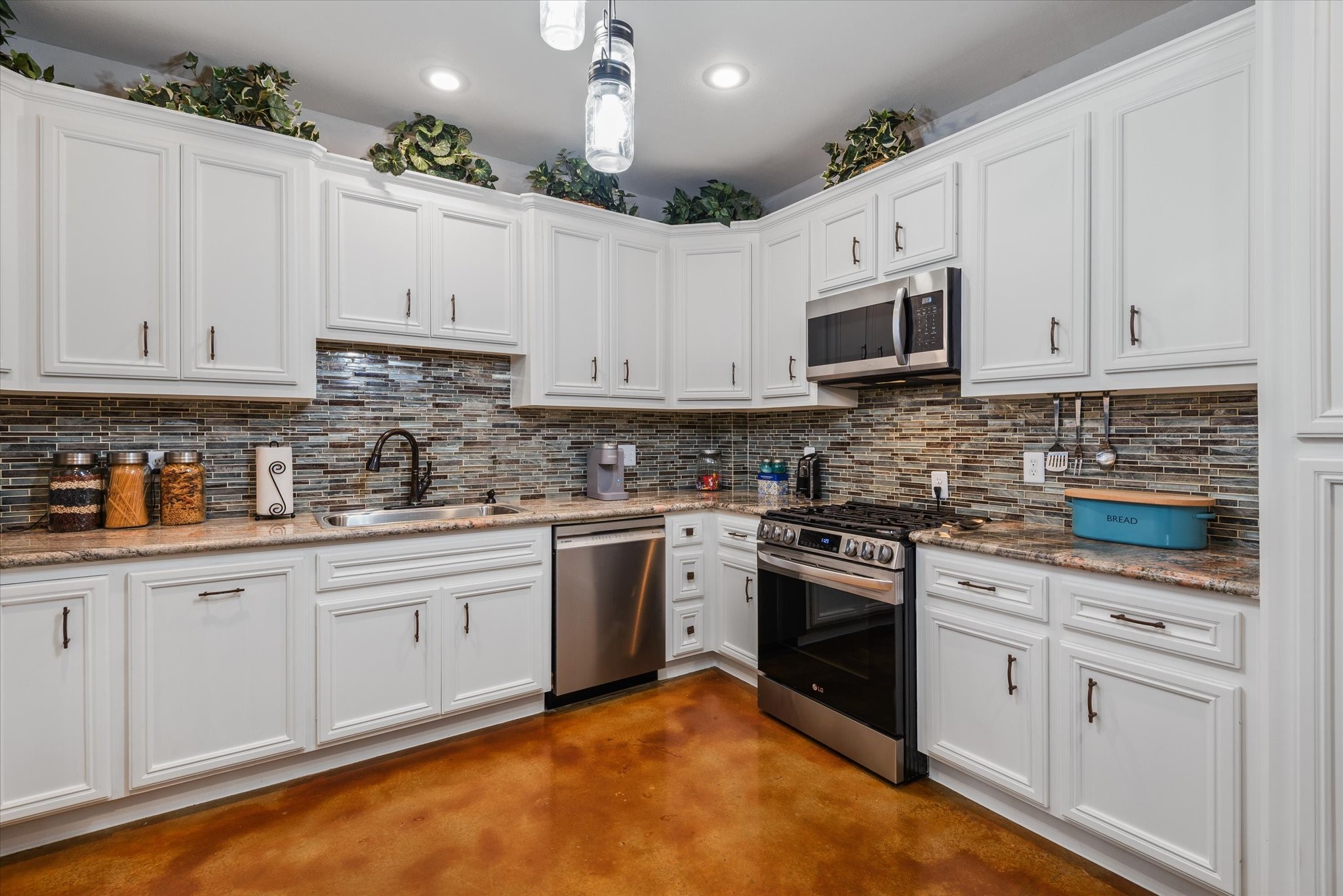 Kitchen with granite countertops, tiled backsplash, stainless-steel appliances, and stained concrete floors.