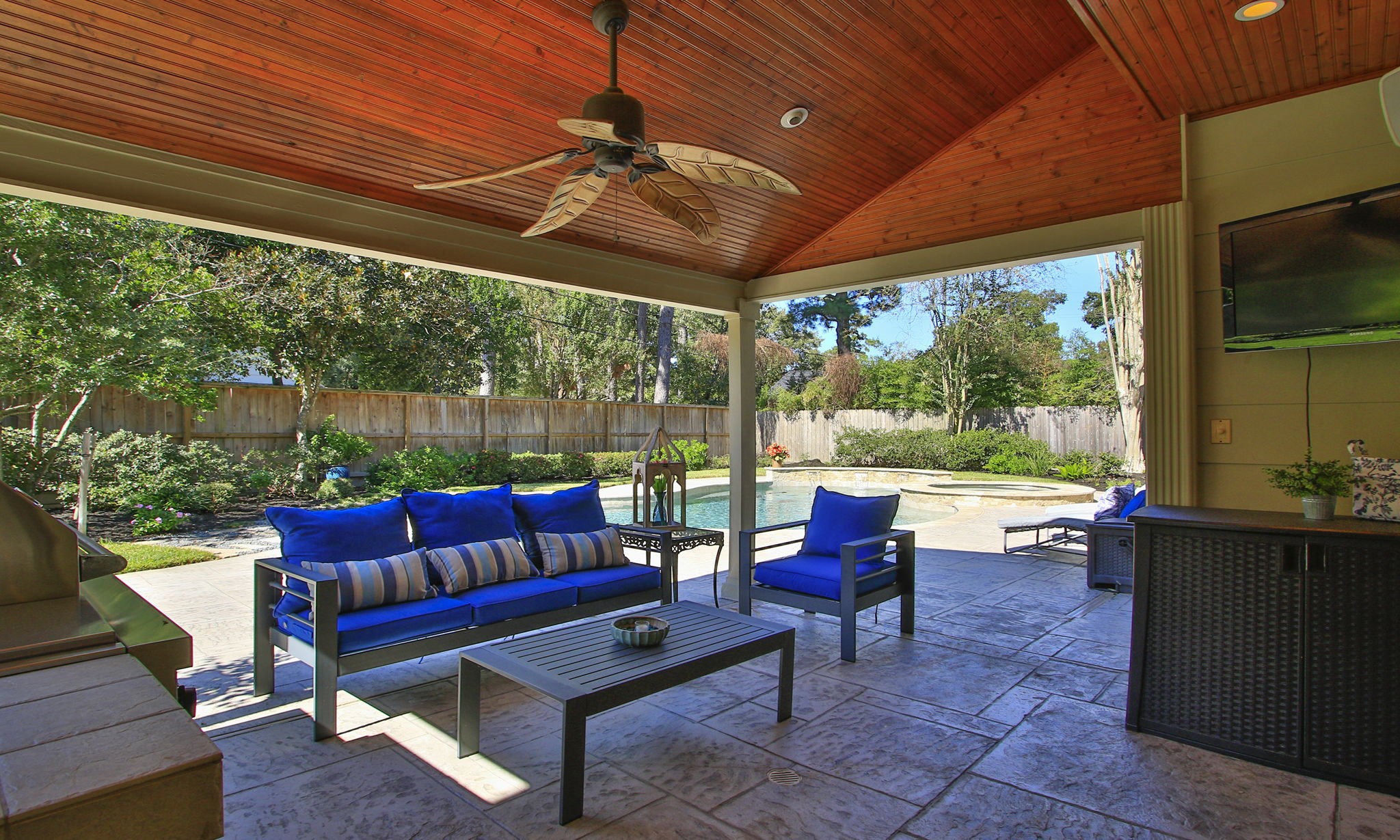 Another view of this stunning covered patio featuring elegant seating, a ceiling fan, and views of a sparkling pool surrounded by lush greenery.
