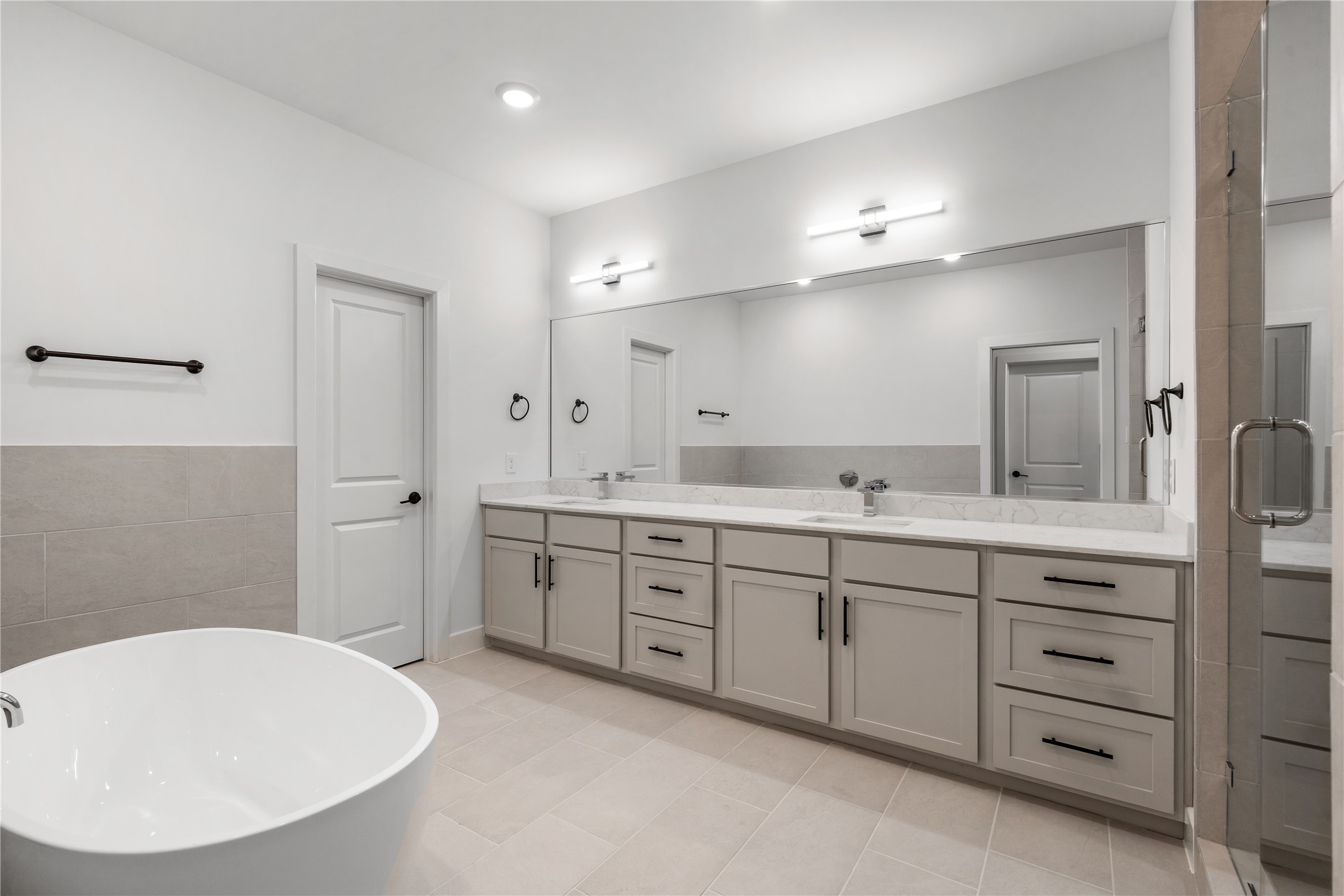 Spa-inspired primary bathroom  standalone soaking tub, quartz double vanity with extended mirror, LED vanity lighting bars, and frameless glass shower enclosure.