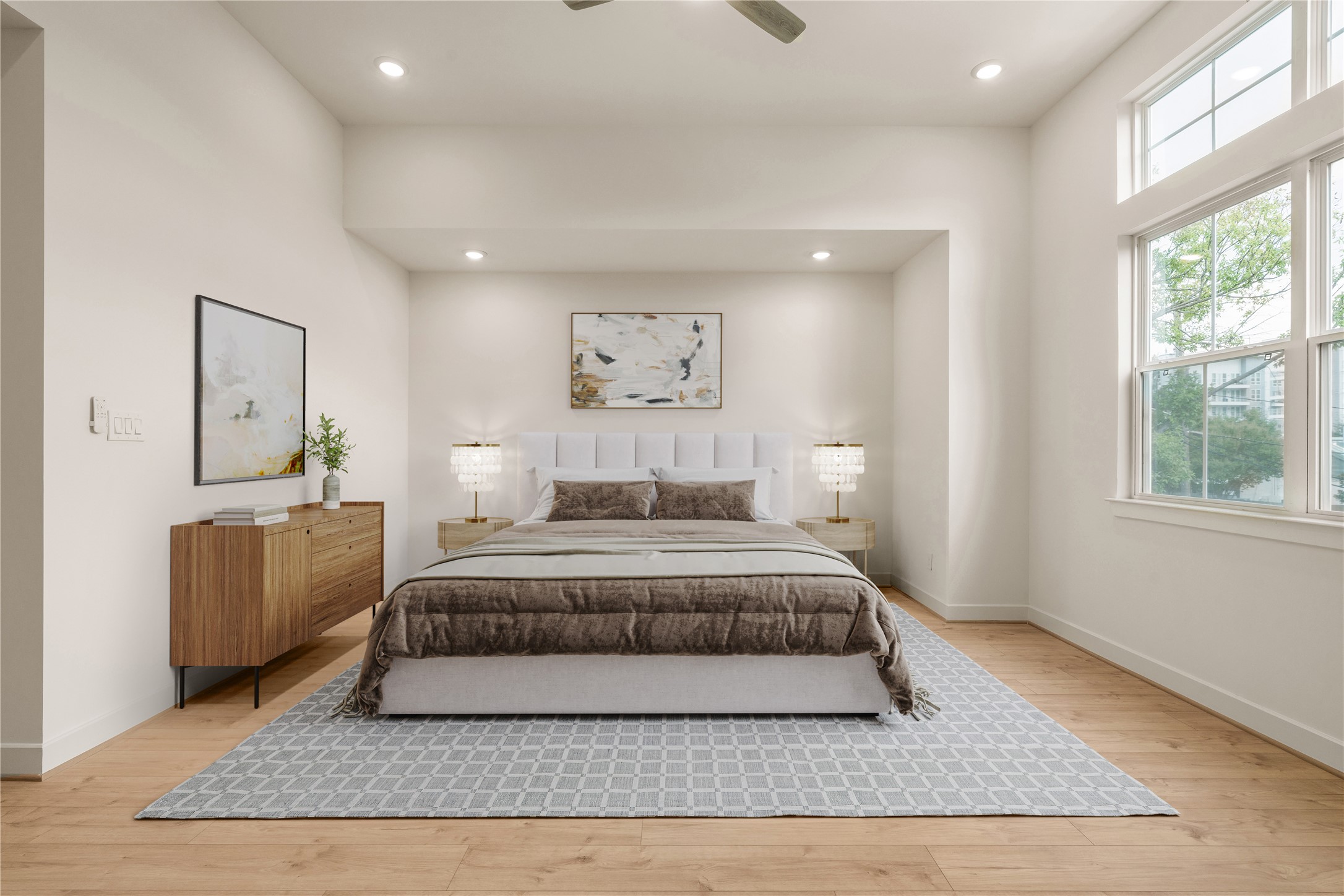 Primary suite sanctuary  symmetrical layout with dual nightstands, elegant table lamps, neutral area rug, and large picture window framing lush neighborhood views.