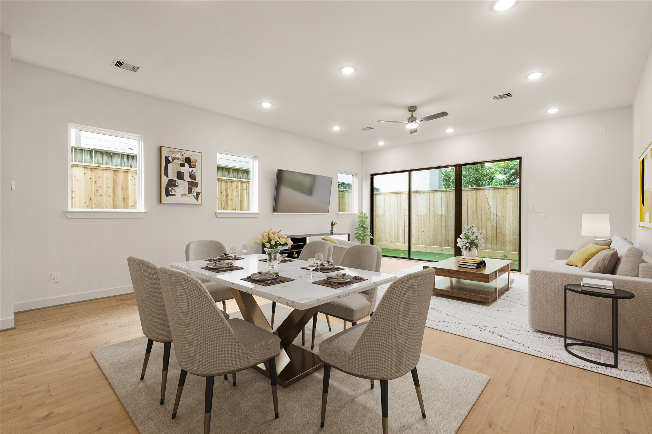 Open-concept living and dining  marble-topped dining table setup, plush sofa seating area, wall-to-wall light wood floors, and oversized sliding glass doors opening to the private yard.