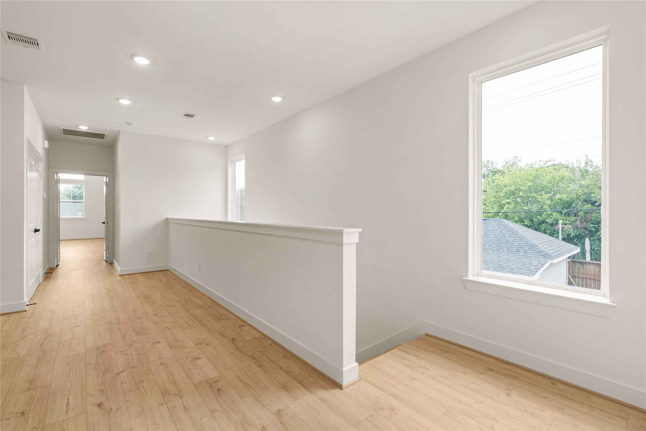 Upper-level landing  bright picture window framing tree-lined views, half-wall partition, and wide-plank wood-look flooring throughout.