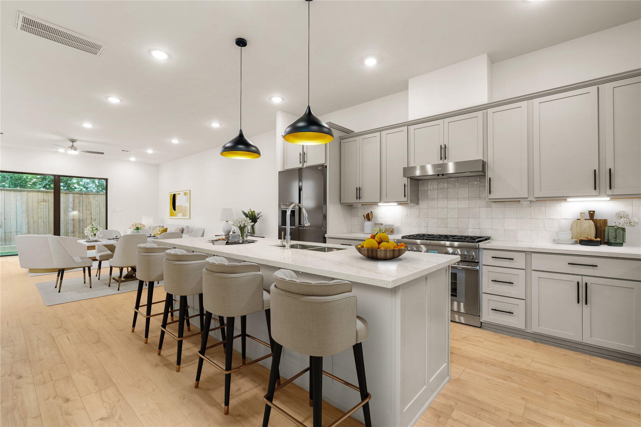 Chef-inspired kitchen design  large prep island featuring elegant bar seating, gas range with stainless vent hood, crisp zellige tile backsplash, and open flow toward the light-filled dining space.