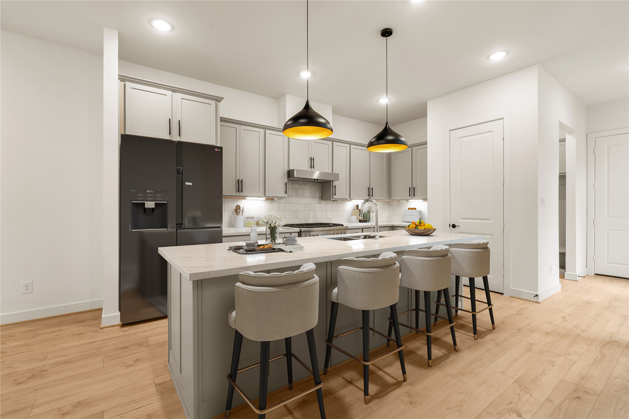 Sleek culinary hub  quartz waterfall island with comfortable counter stool seating, statement drop lighting, integrated stainless appliances, and wide-plank wood-look flooring.