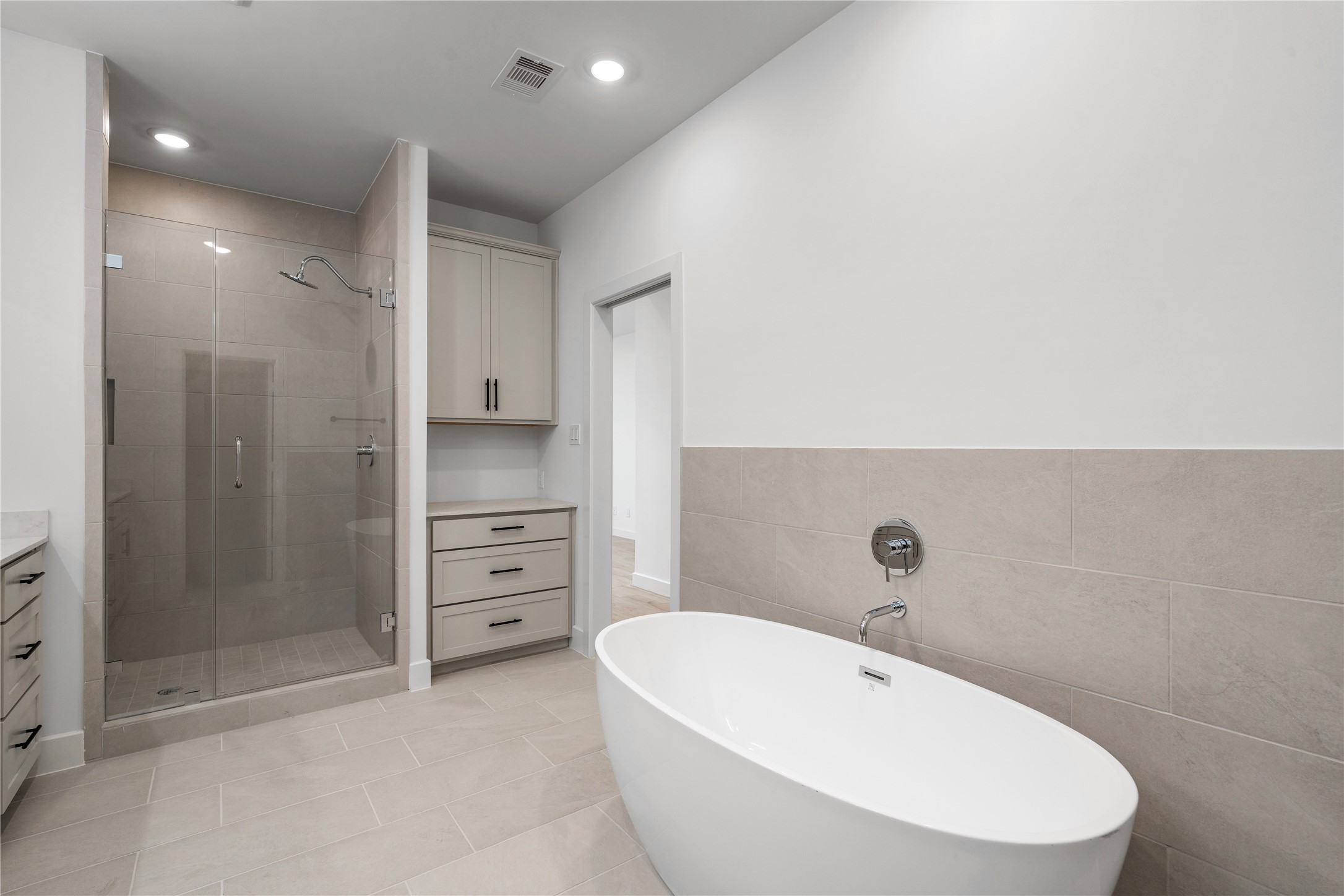 Primary bathroom oasis  freestanding soaking tub set against tile wainscoting, walk-in tile shower, and built-in storage drawers.