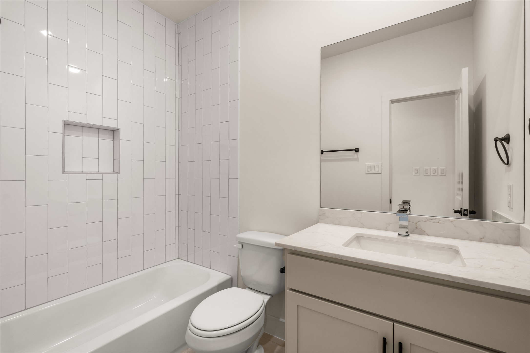 Secondary bath  designer white vertical stack tile surround, inset storage niche, deep soaking tub, and quartz-topped vanity.