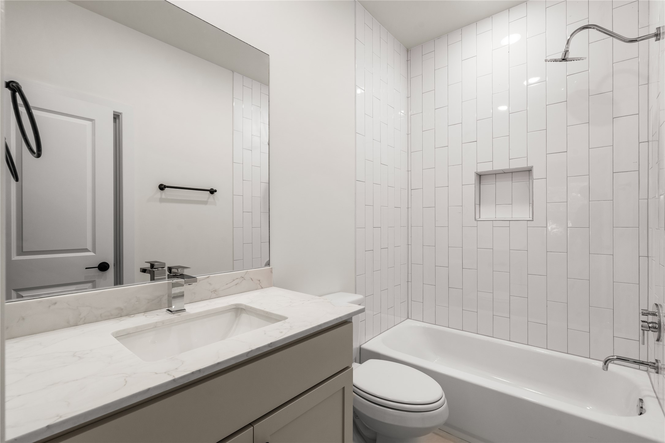 Guest bath setup  vertical stack subway tile surround, built-in shampoo niche, quartz-topped vanity, and clean black hardware accents.