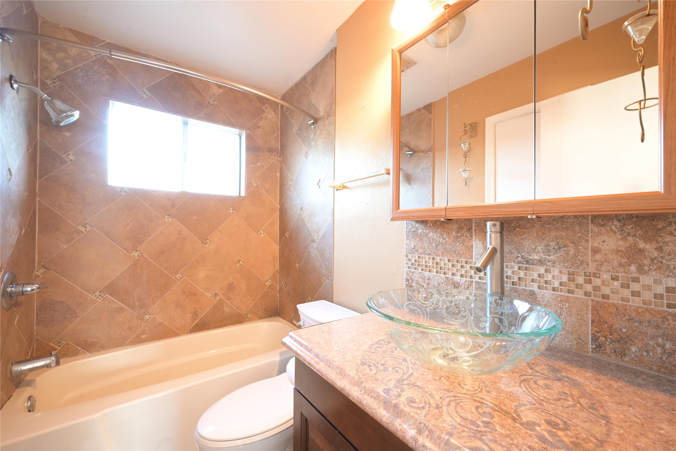 Floor-to-ceiling tile and a glass vessel sink with mosaic accents