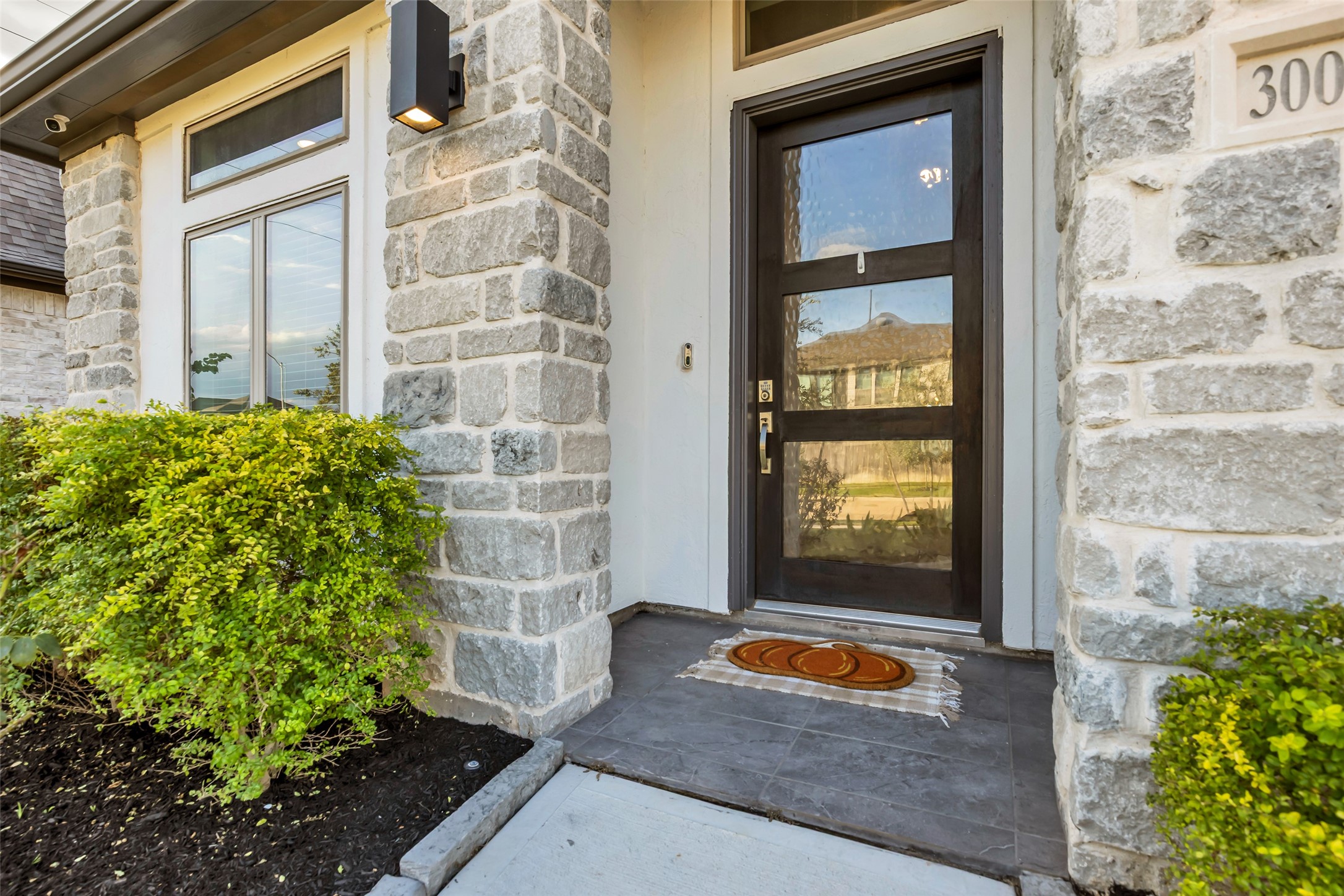 Charming Stonework Grace Your Entryway Along w/ A Sleek, Modern Door, Framed By Lush Greenery For A Welcoming First Impression.