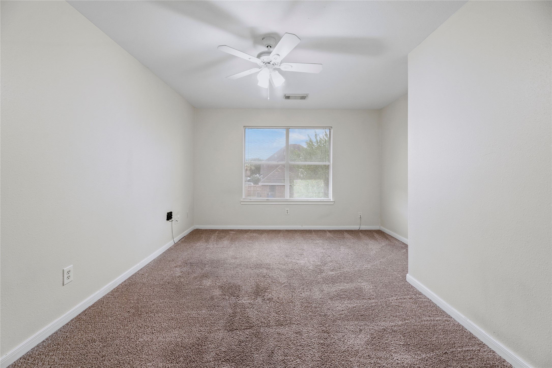 This secondary bedroom pairs a window and ceiling fan with open floor space, giving you room to arrange a bed, desk or your own preferred setup.