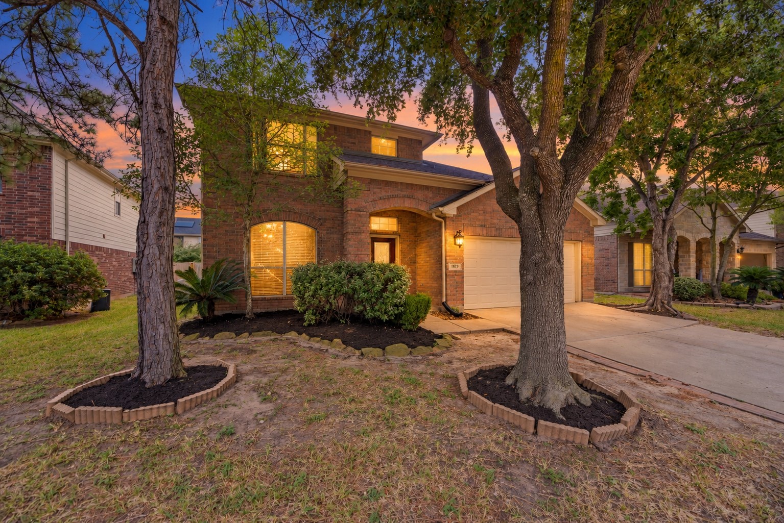 A closer look at the mature front trees and brick facade, with a covered entry set beside the garage and planting beds along the home. A closer look at the mature front trees and brick facade, with a covered entry set beside the garage and planting beds along the home.