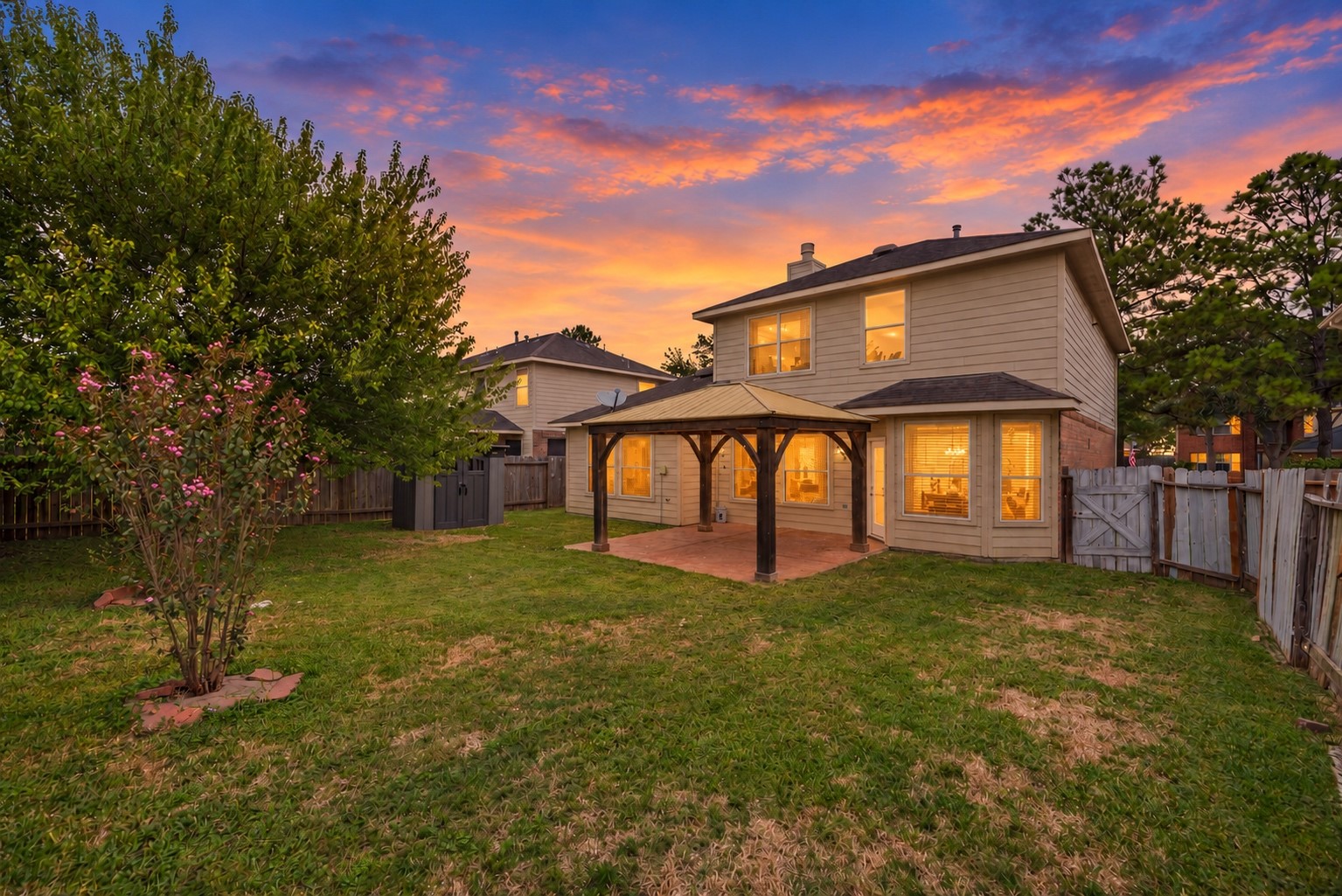 Twilight view of the backyard with the natural seasonal lawn, existing gazebo-covered patio and rear of the home.