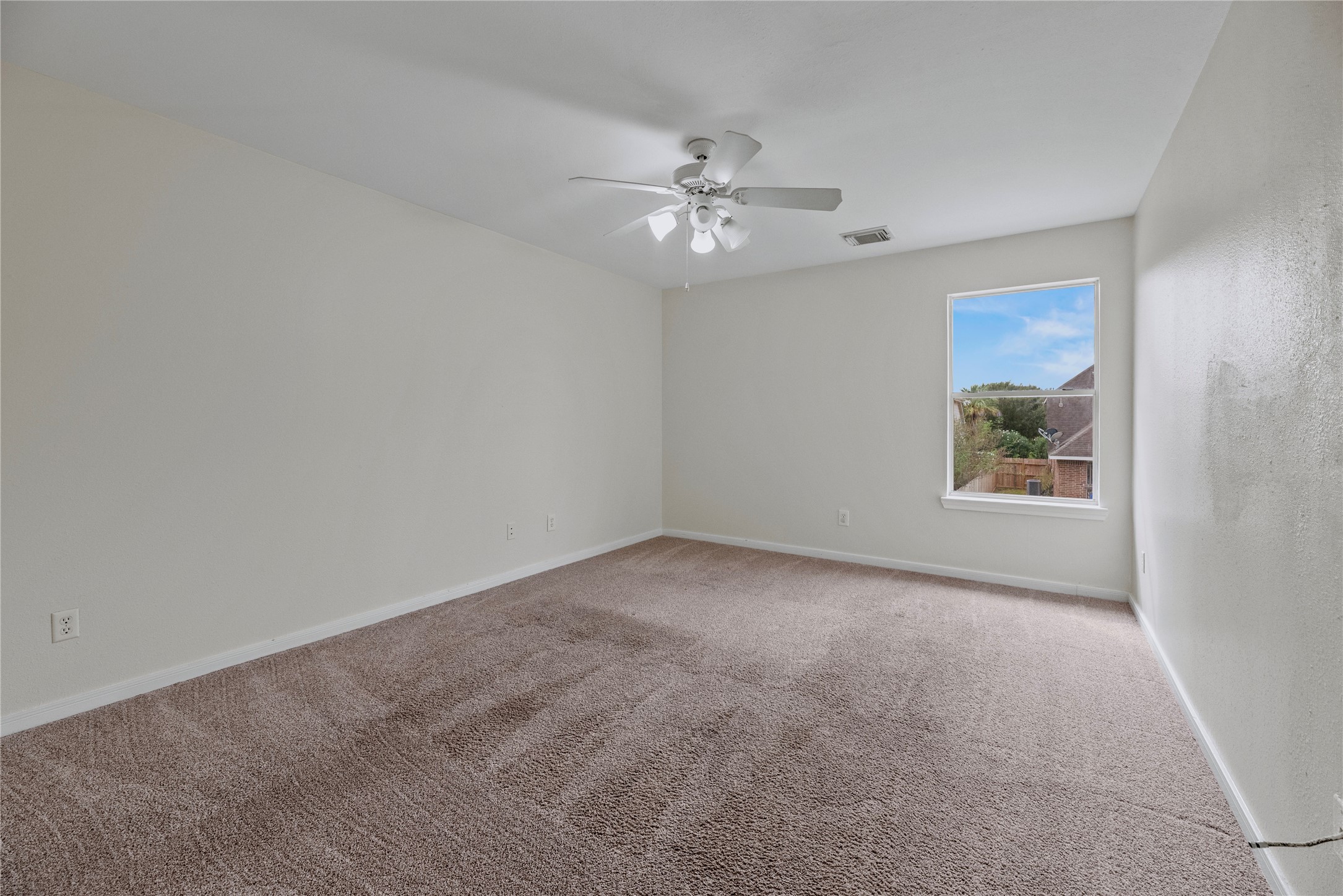 A broad wall and window give this secondary bedroom a straightforward furniture layout, with a ceiling fan overhead for added comfort.