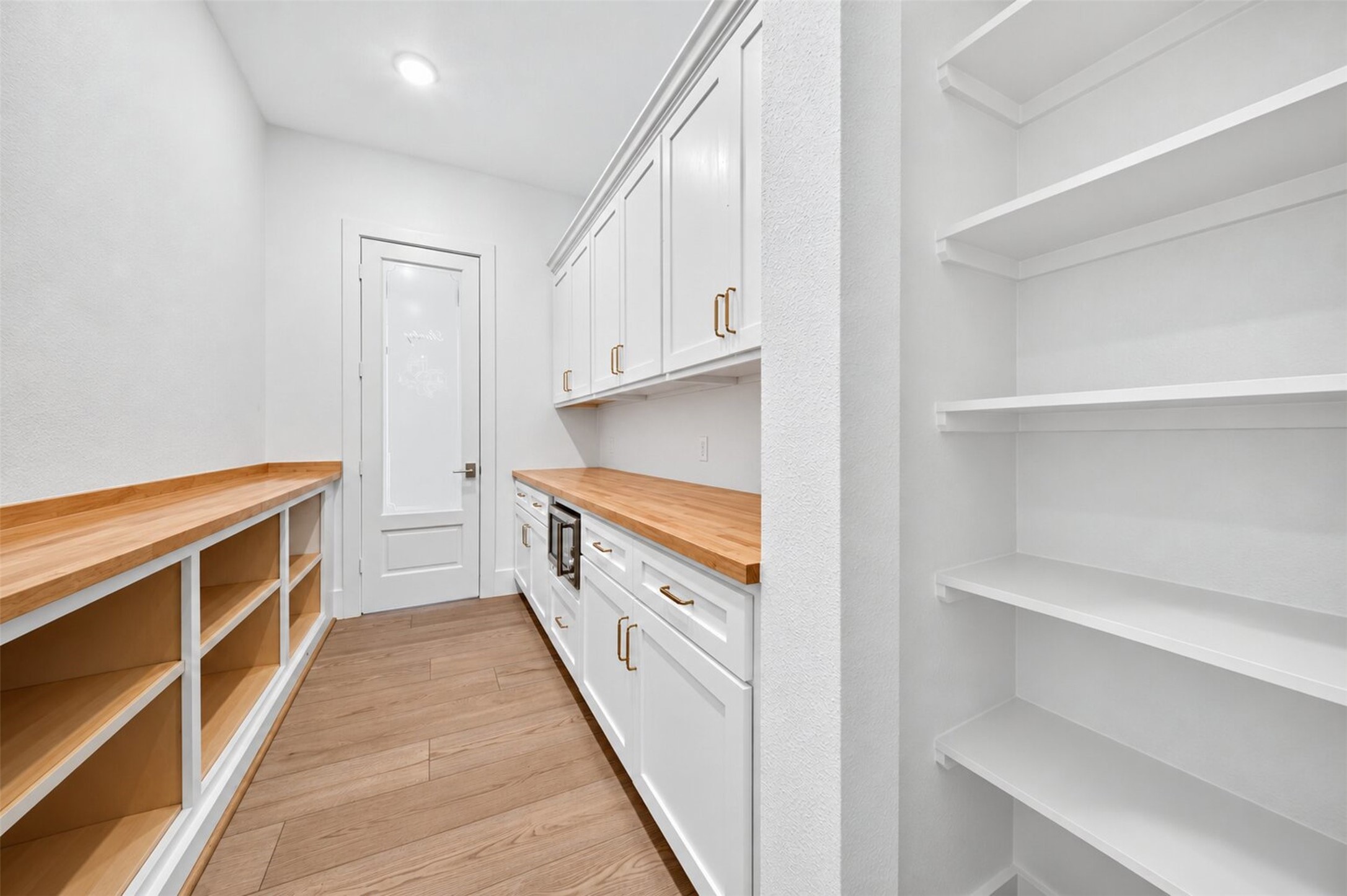 The walk-in pantry pairs wraparound shelving with white cabinetry, butcher-block counters for prep and storage.