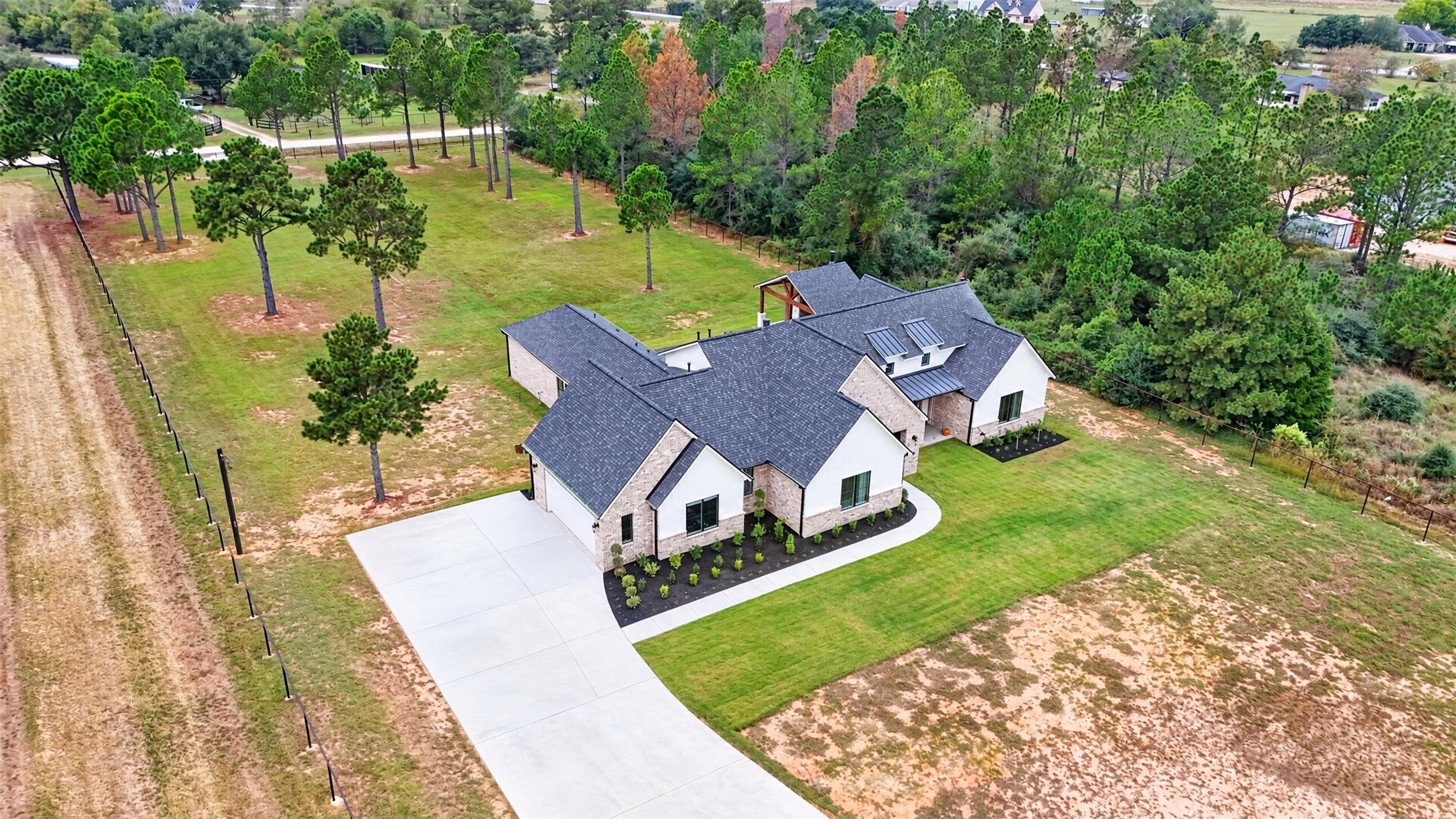 A drone angle captures the home's varied rooflines, driveway, broad lawn, and tree-lined acreage.