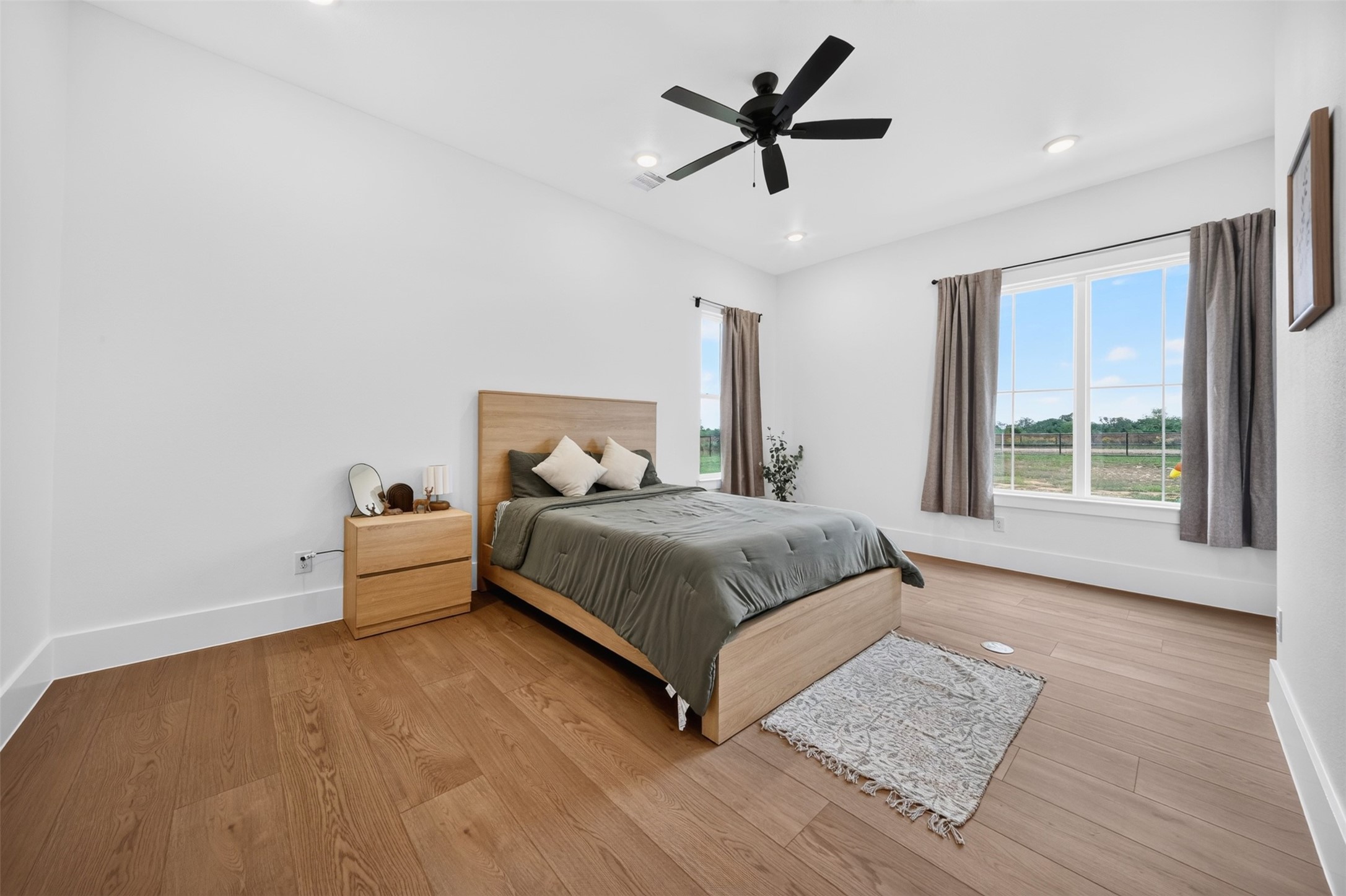 This secondary bedroom looks out over the property through wide windows, with wood-look floors and a ceiling fan completing the space.