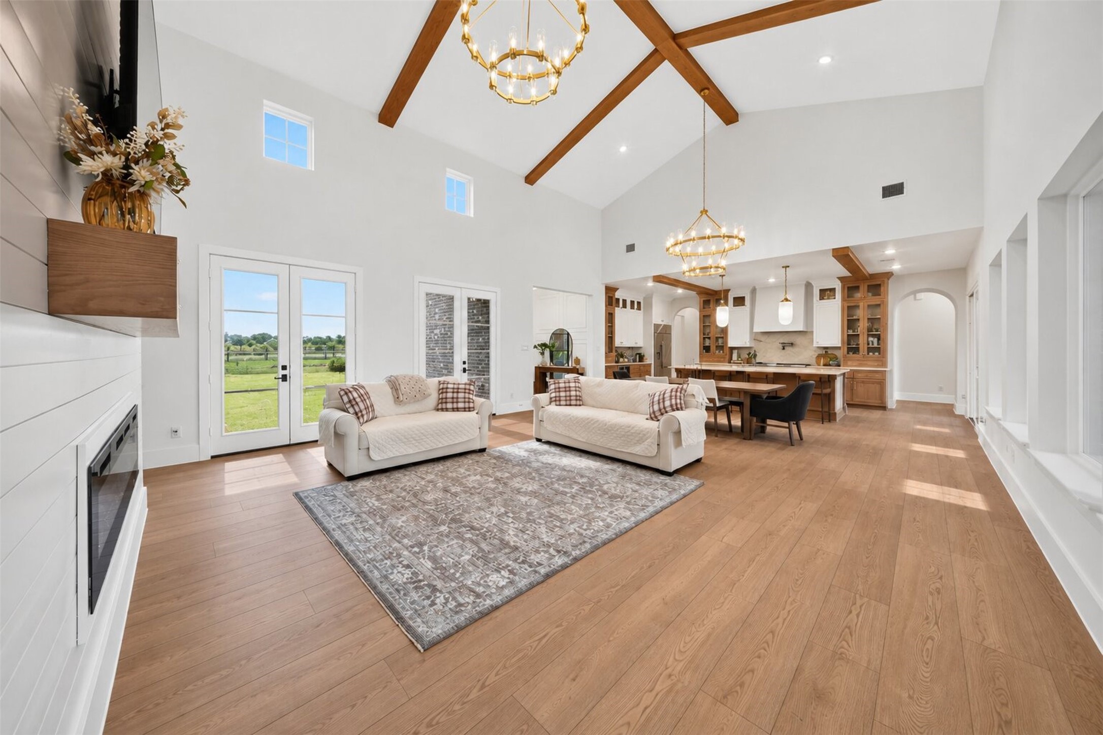 The family room flows into the kitchen beneath exposed beams, while tall windows carry the open sightline out toward the yard.