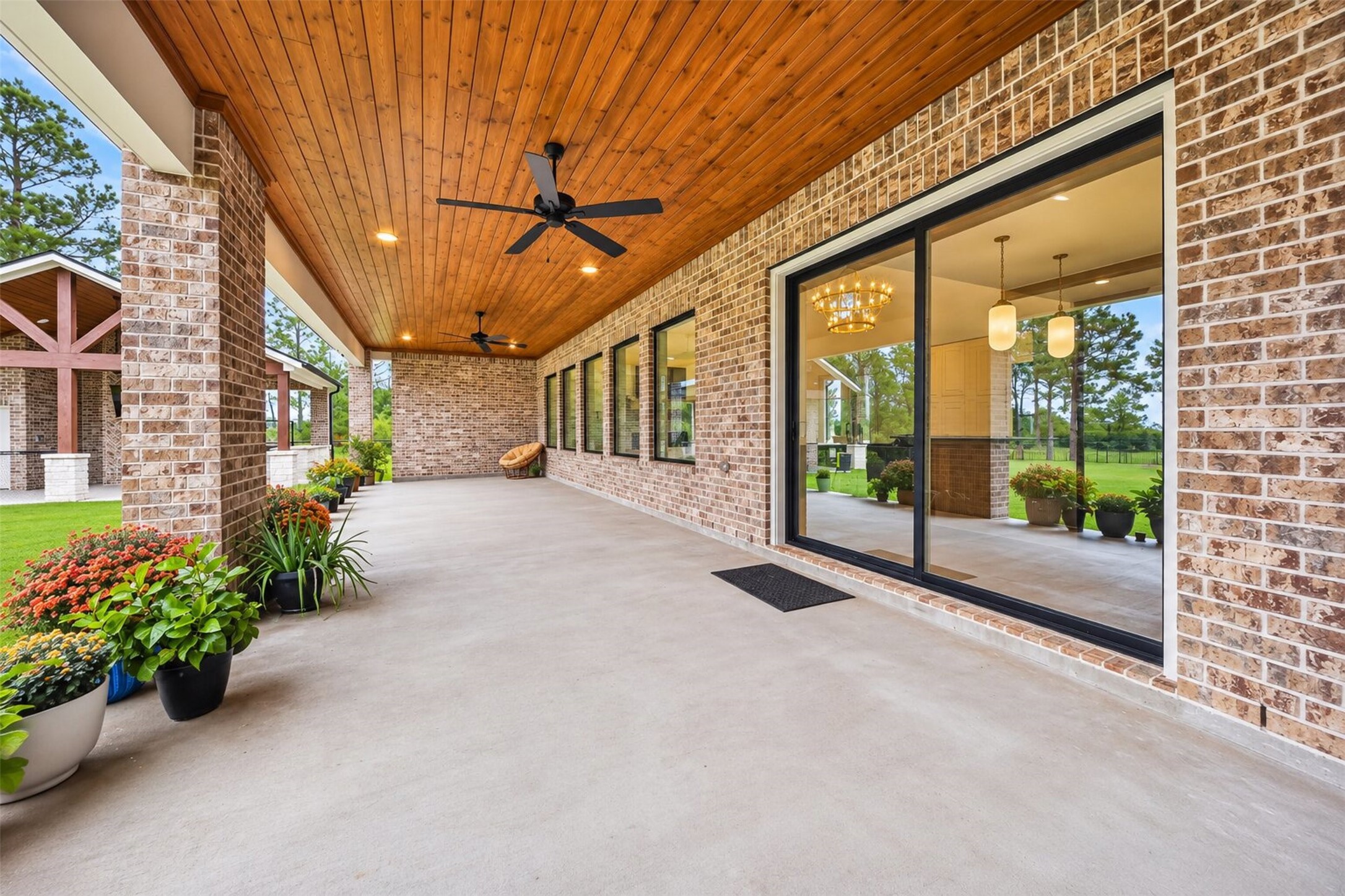 The covered patio follows the home's brick rear wall, with wide windows and glass doors connecting the interior to the yard.